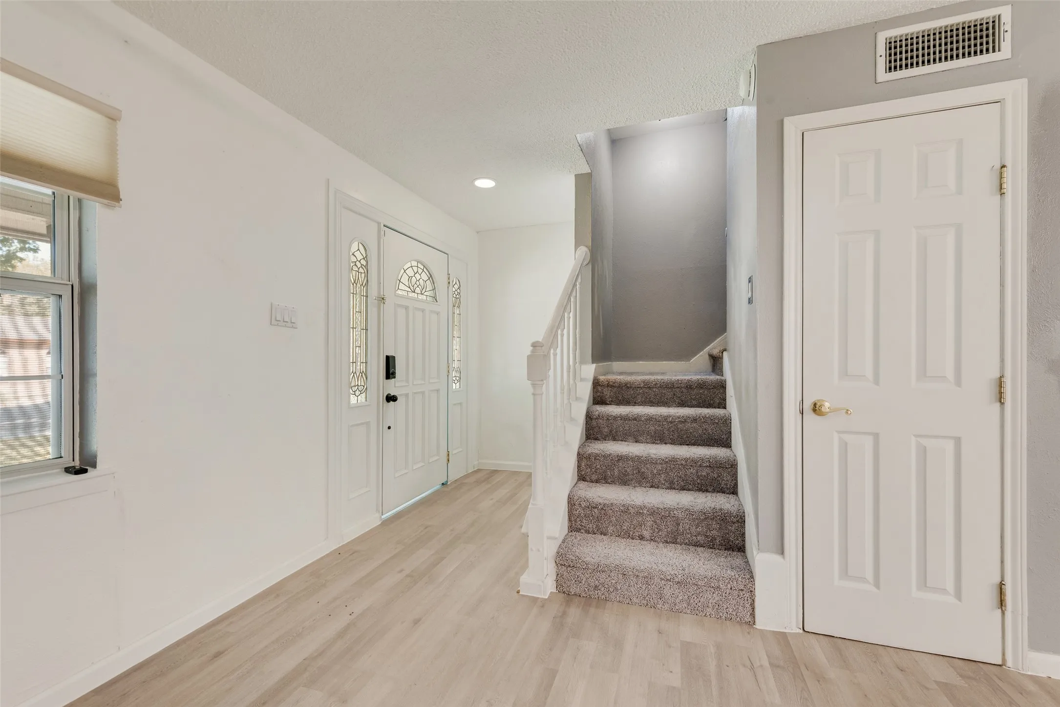 Entryway featuring wood-finish flooring, a white paneled entry door with decorative glass inserts, and a carpeted staircase with a white railing