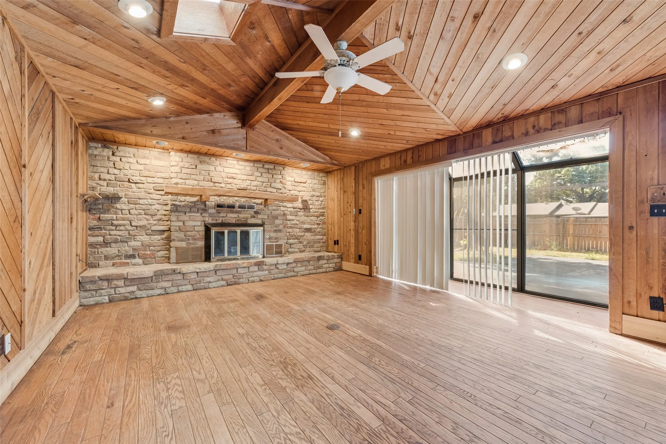 Vaulted wood-paneled ceiling with skylight, wood-finish flooring, stone-faced fireplace, and sliding glass doors