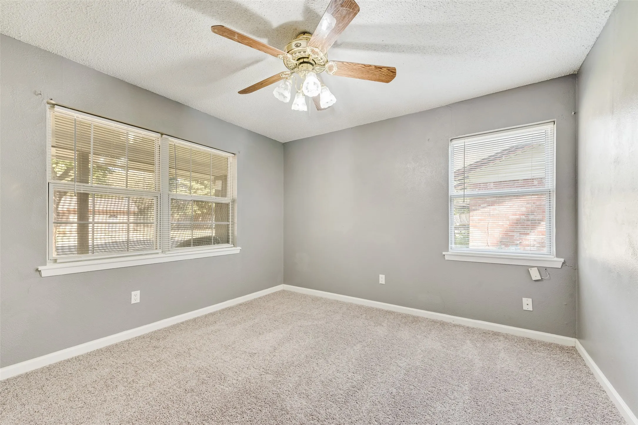 Neutral gray wall paint with white trim, light-colored carpeting, multiple windows, and a ceiling fan with light fixture