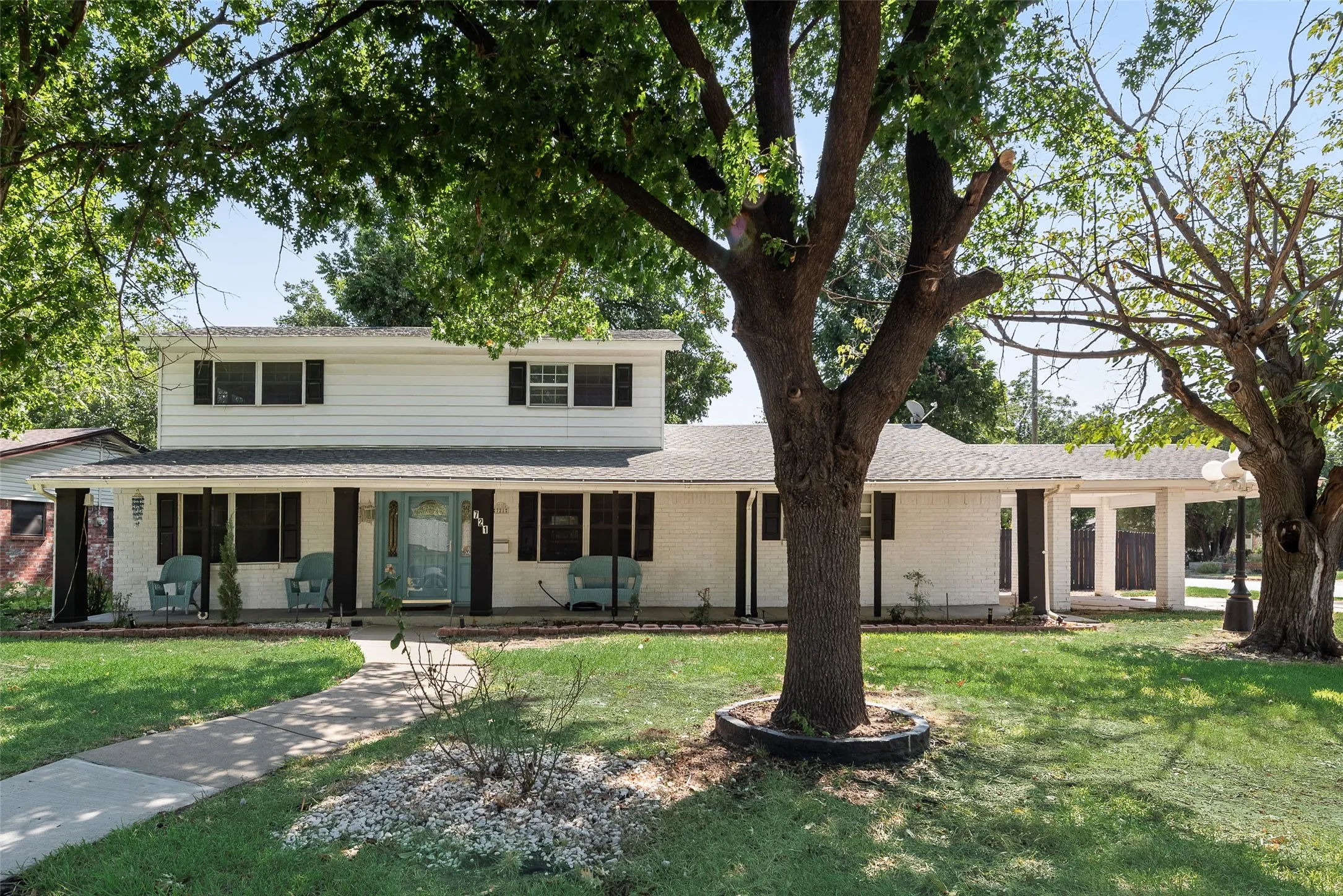 Two-story white exterior, covered front porch, light blue front door, black window shutters, and a covered carport structure