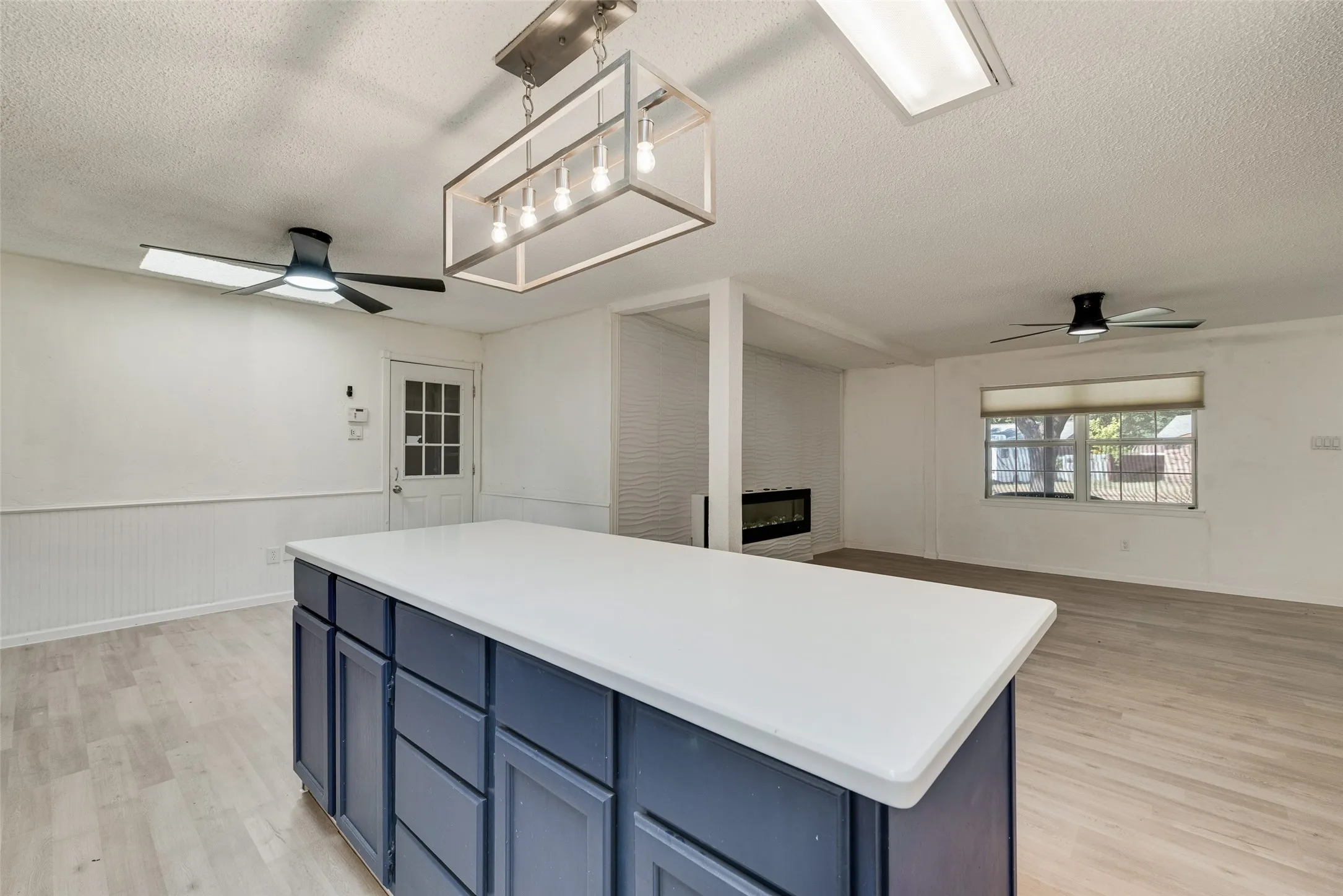 Open-concept living space featuring wood-finish flooring, a contemporary island with storage, modern ceiling fans, and a built-in electric fireplace
