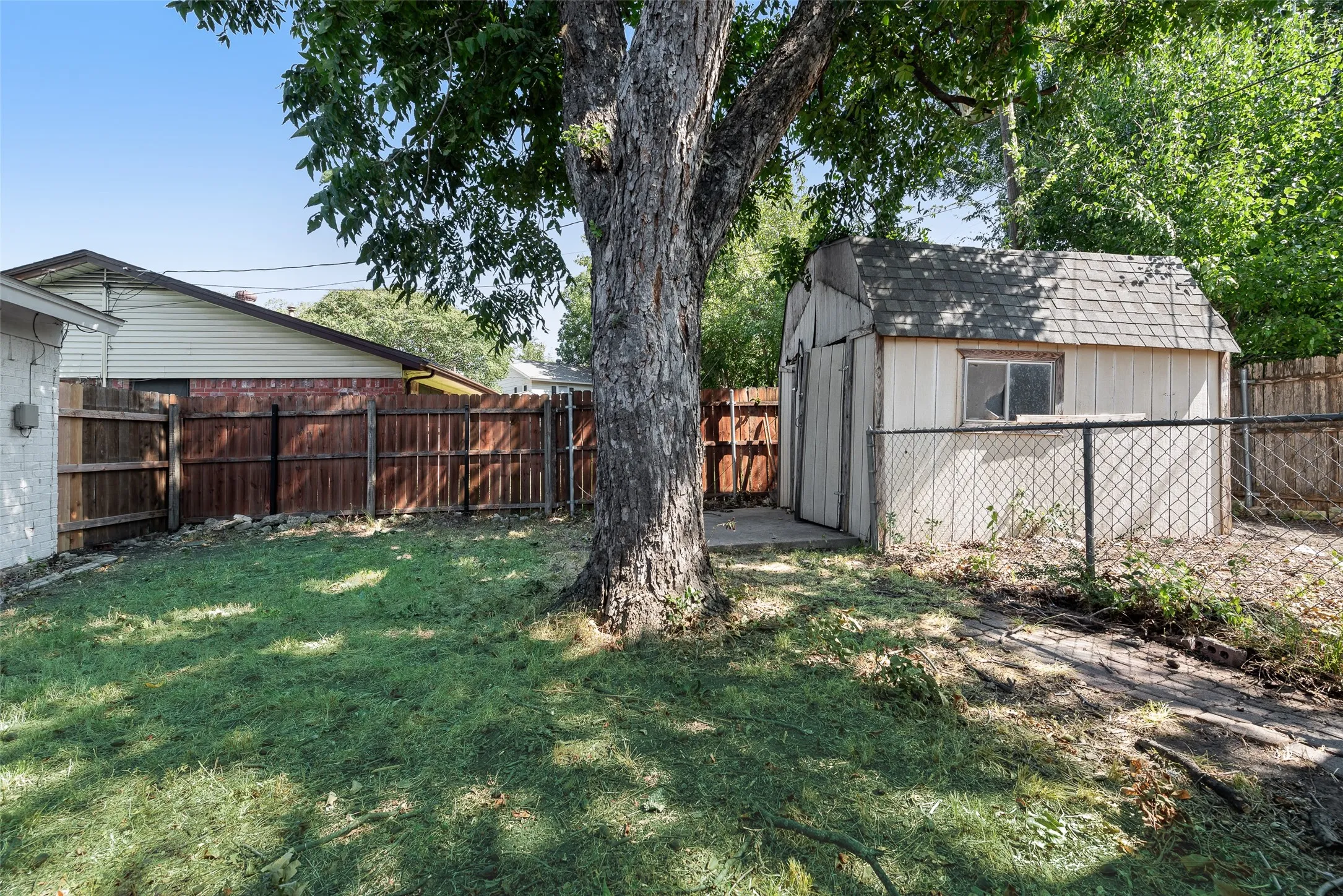 Fenced backyard featuring a mature tree, wood fencing, and a storage shed