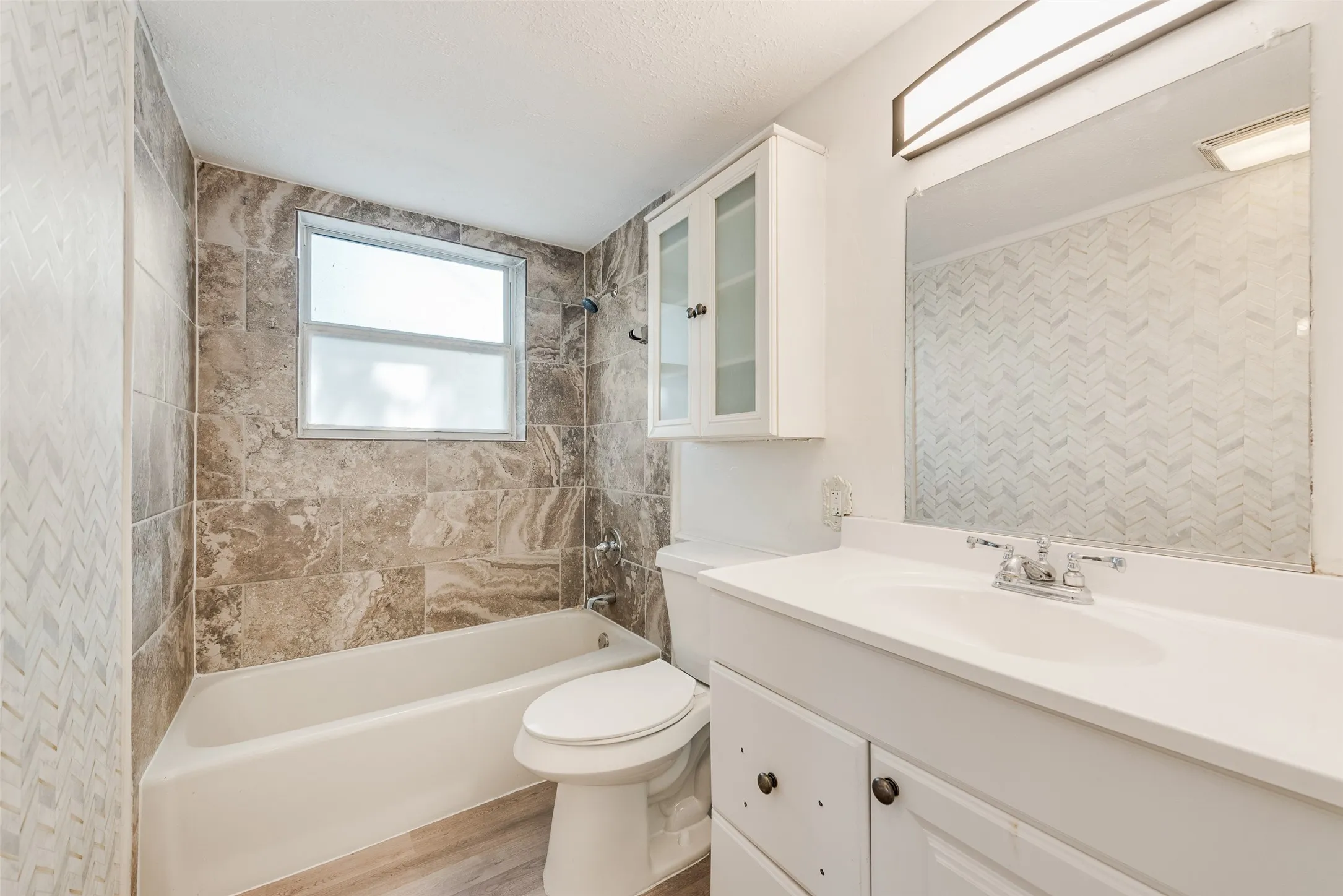 Bathroom featuring a tub, tiled shower surround, window, vanity with integrated sink, and overhead storage cabinetry