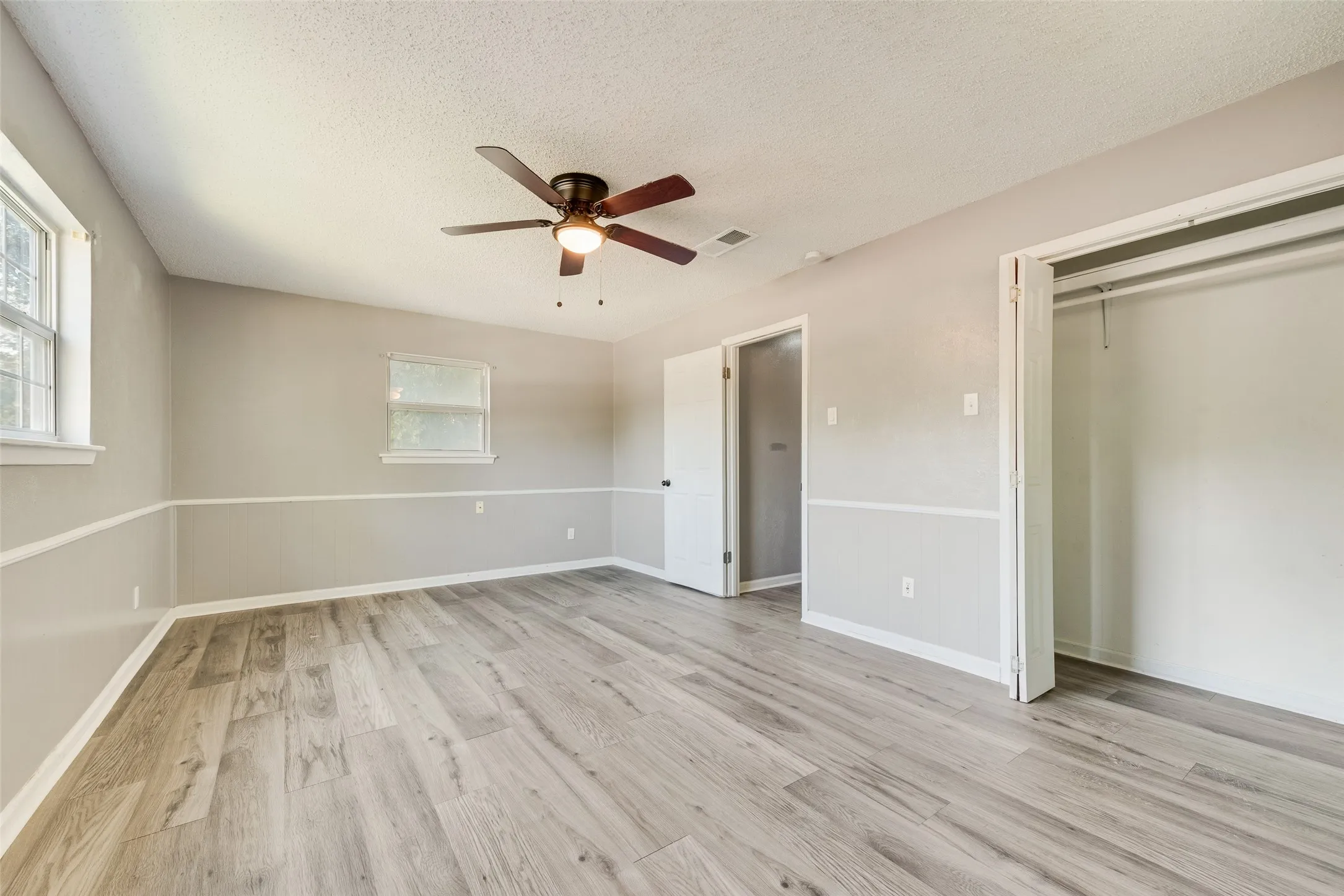 Wood-finish flooring, ceiling fan with light fixture, multiple windows, and a closet with bifold doors
