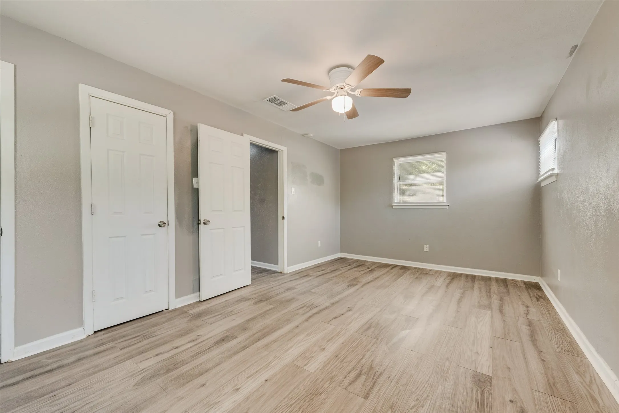 Spacious room featuring wood-finish flooring, two windows, two paneled doors, and a ceiling fan