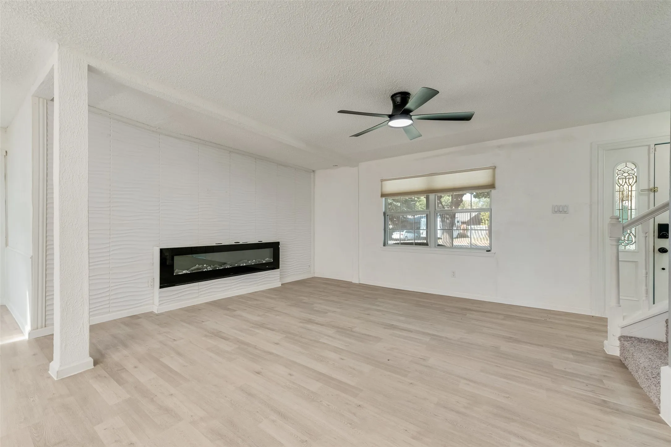 Wood-finish flooring, a contemporary linear fireplace, and a ceiling fan with integrated lighting