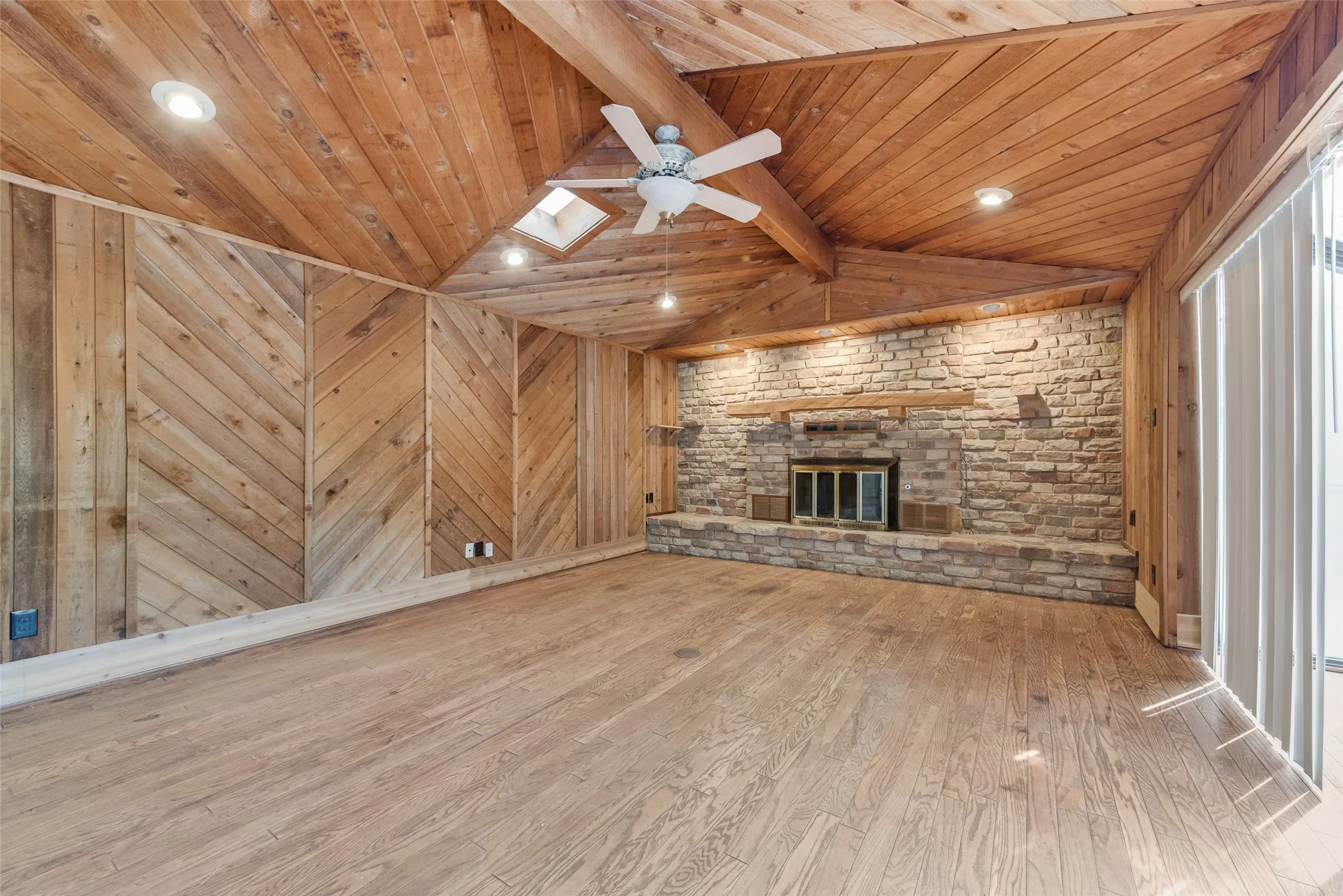 Vaulted wood-paneled ceiling, exposed wooden beams, wood-finish flooring, stone-clad fireplace, and a skylight