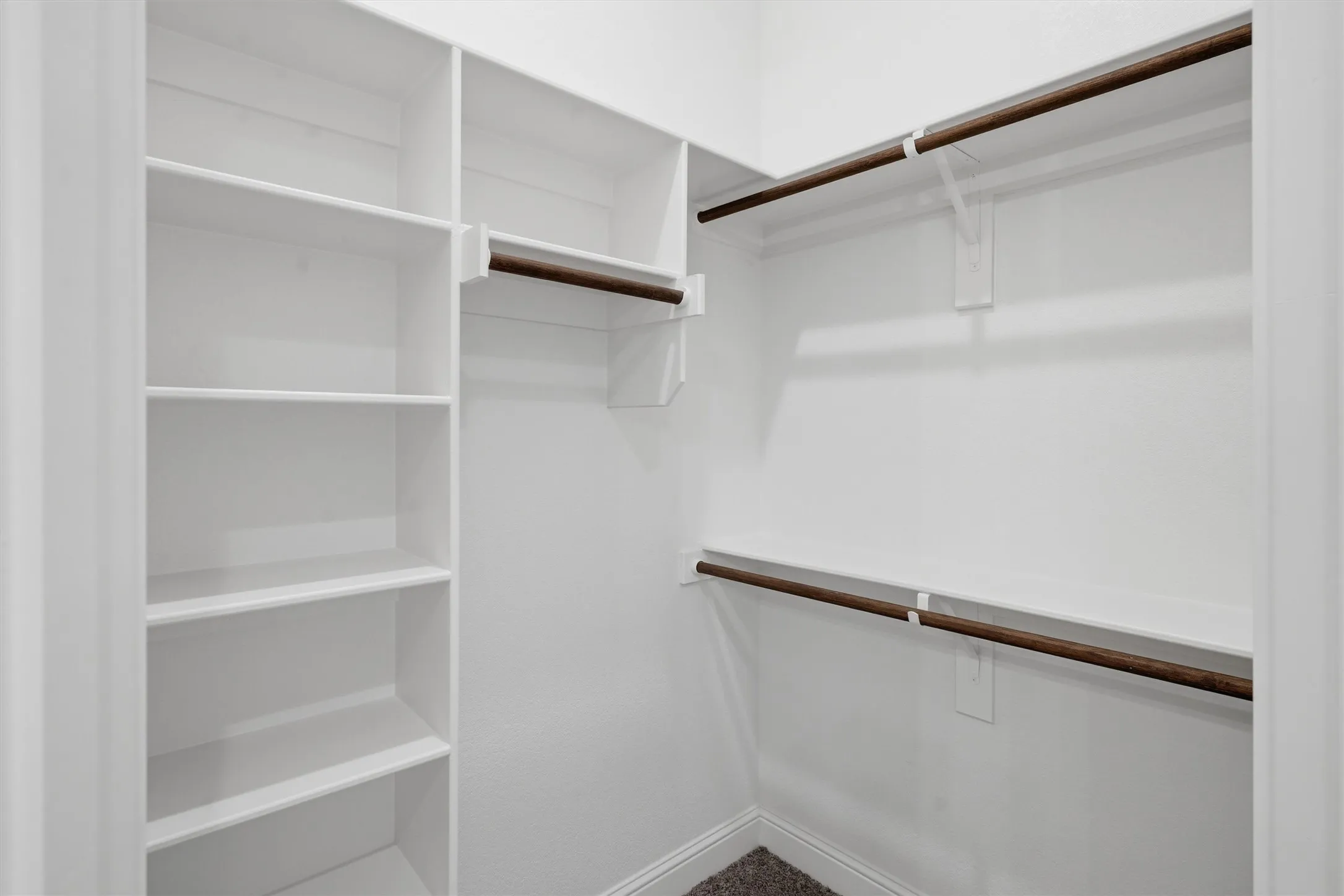 Walk-in closet featuring built-in shelving, white walls, and wood-finish hanging rods