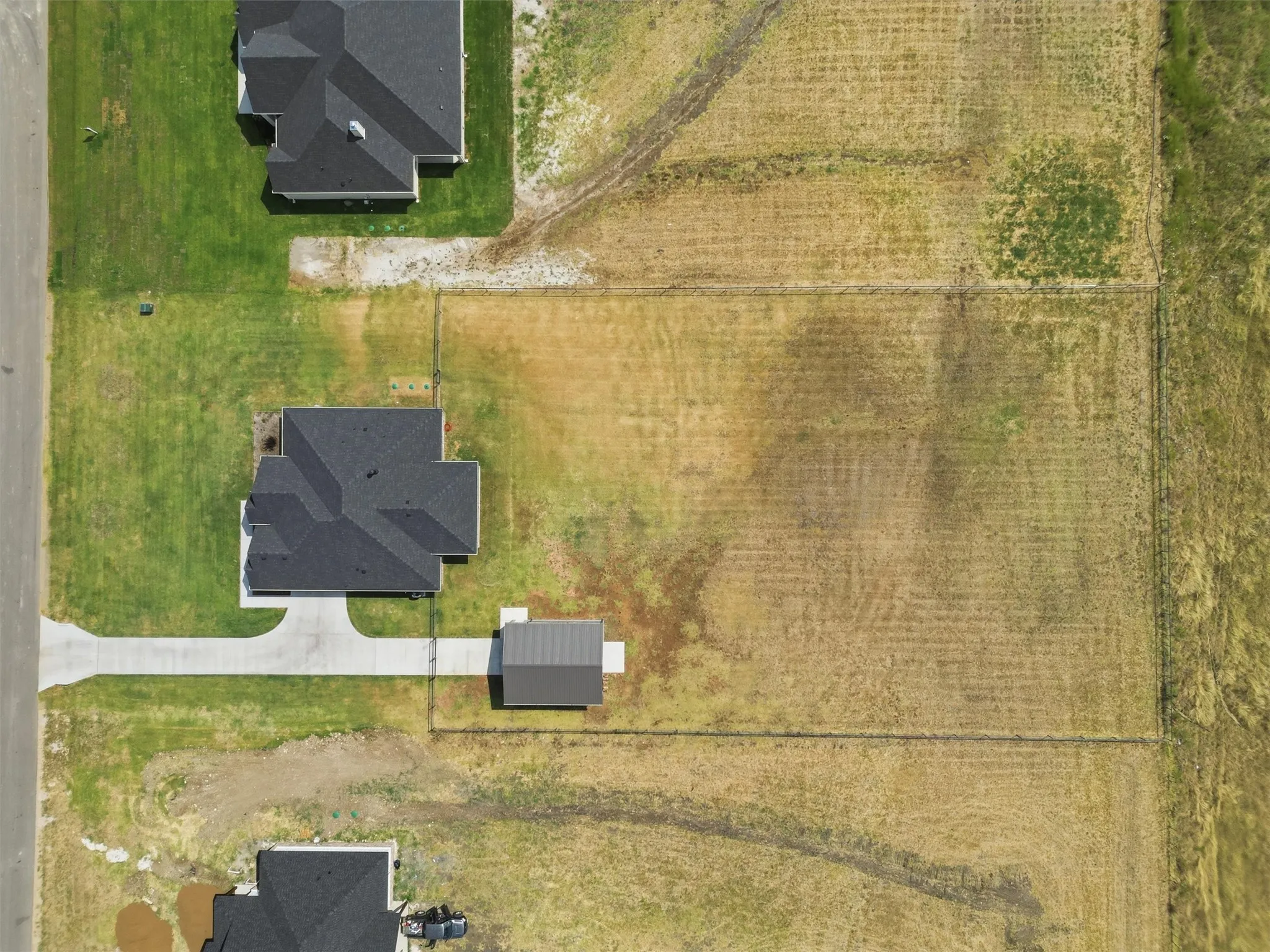 Expansive lot featuring a single-story residence with a dark shingle roof, a detached auxiliary structure, and a concrete driveway