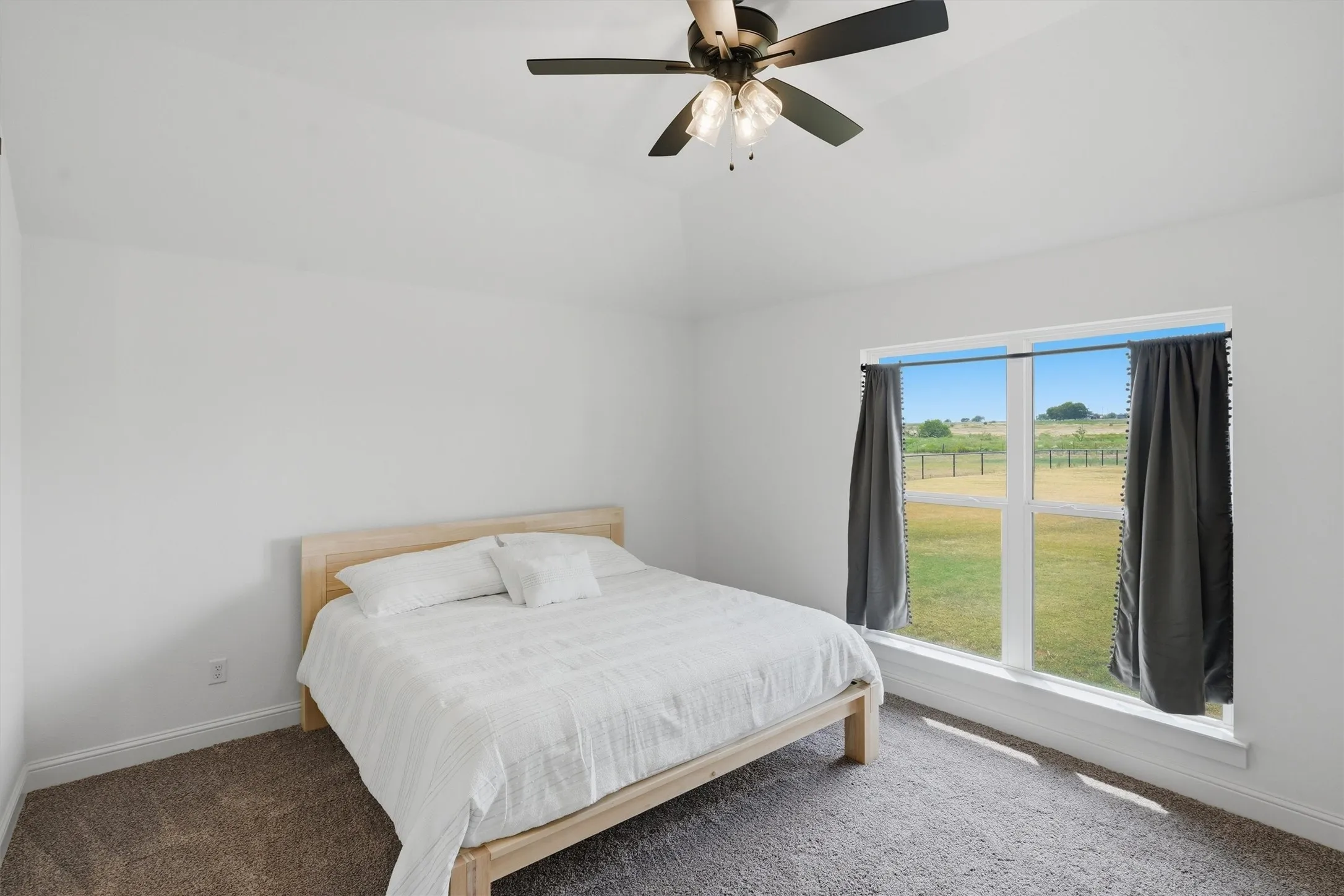 Vaulted ceiling with a ceiling fan, carpeted flooring, and a large window with a distant landscape