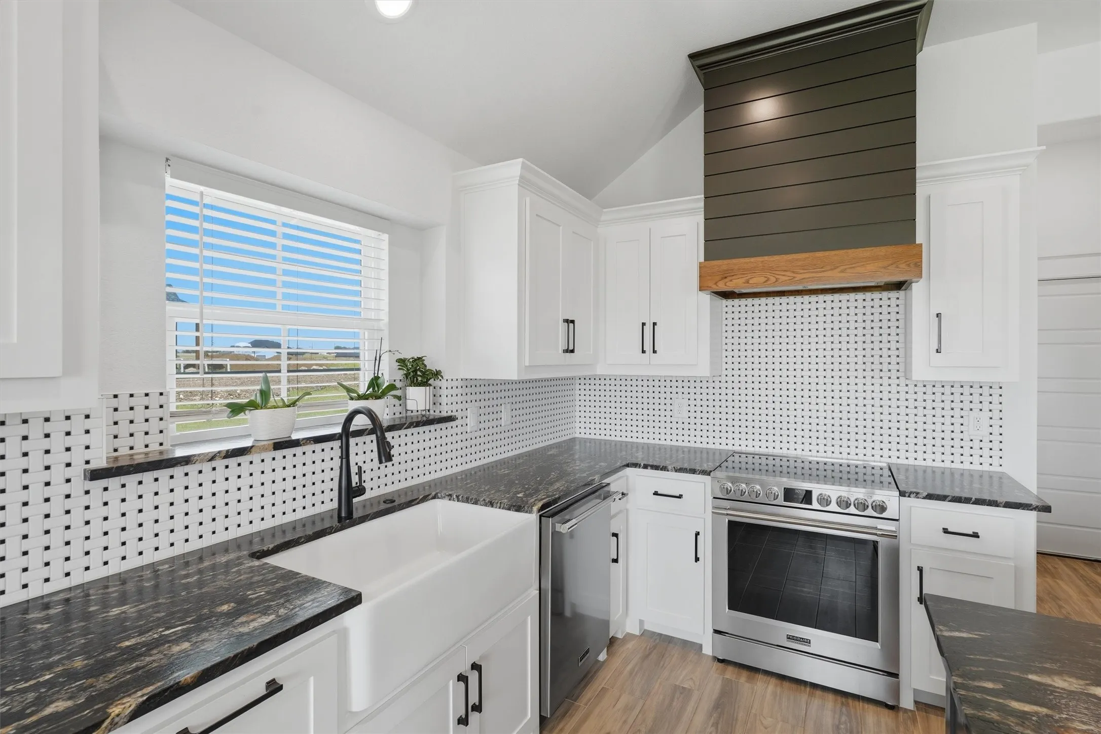 Stainless steel appliances, wood-finish flooring, white cabinetry, dark stone countertops, and a farmhouse sink