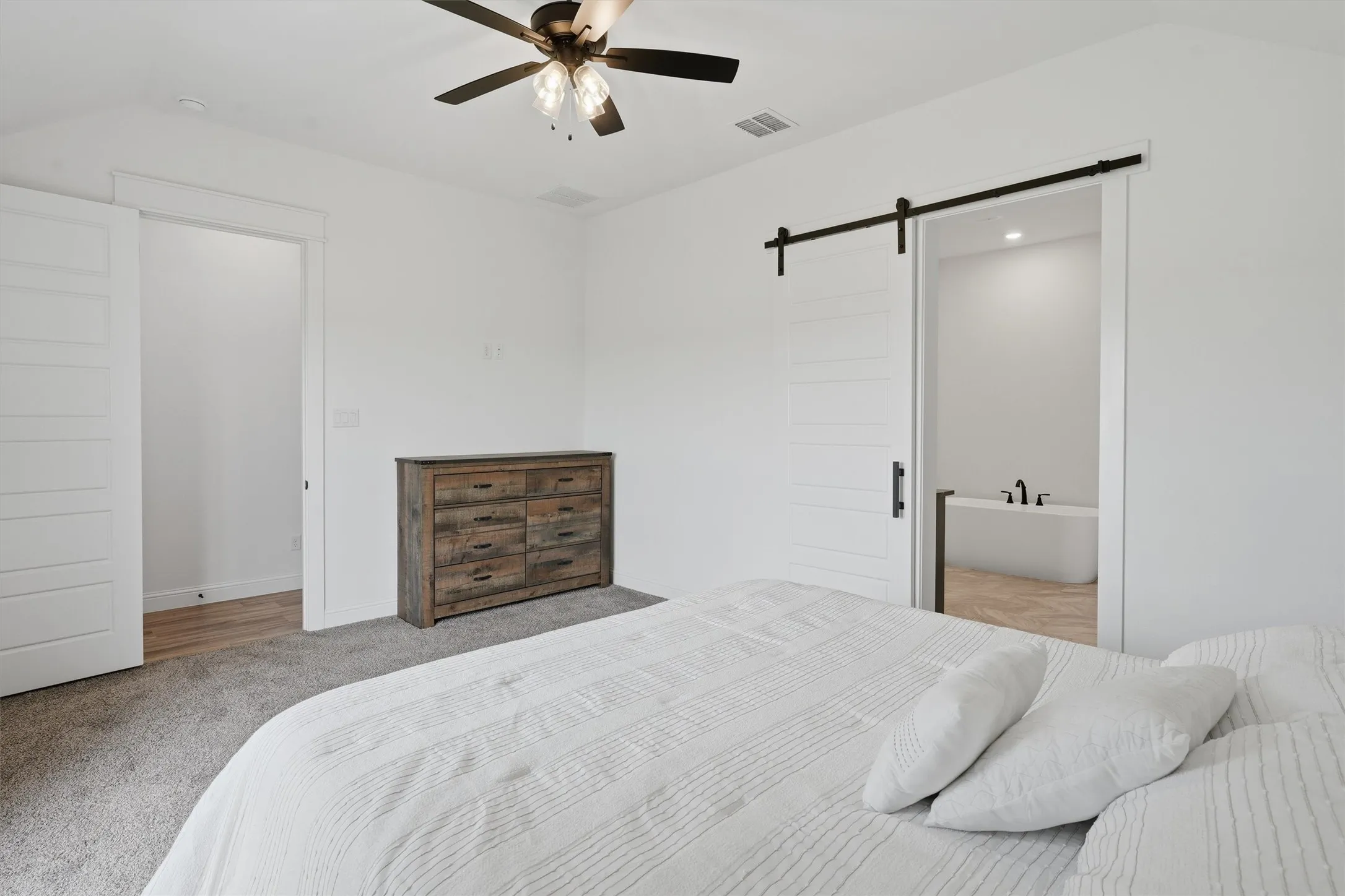 Ceiling fan, white barn door, freestanding tub, recessed lighting, and wood-finish flooring