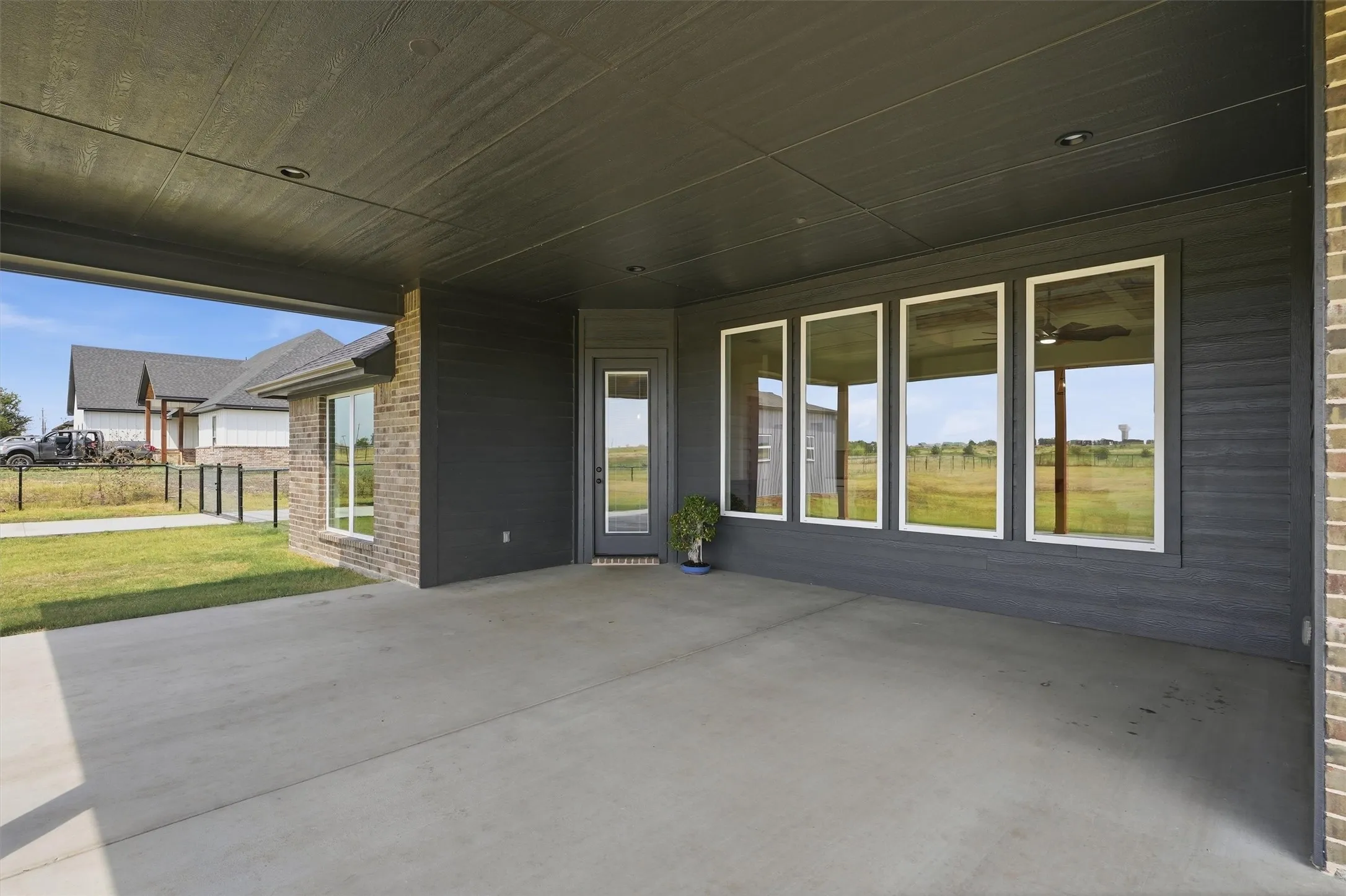 Covered patio with a concrete surface, featuring recessed lighting, a brick exterior wall, and multiple large windows with white frames