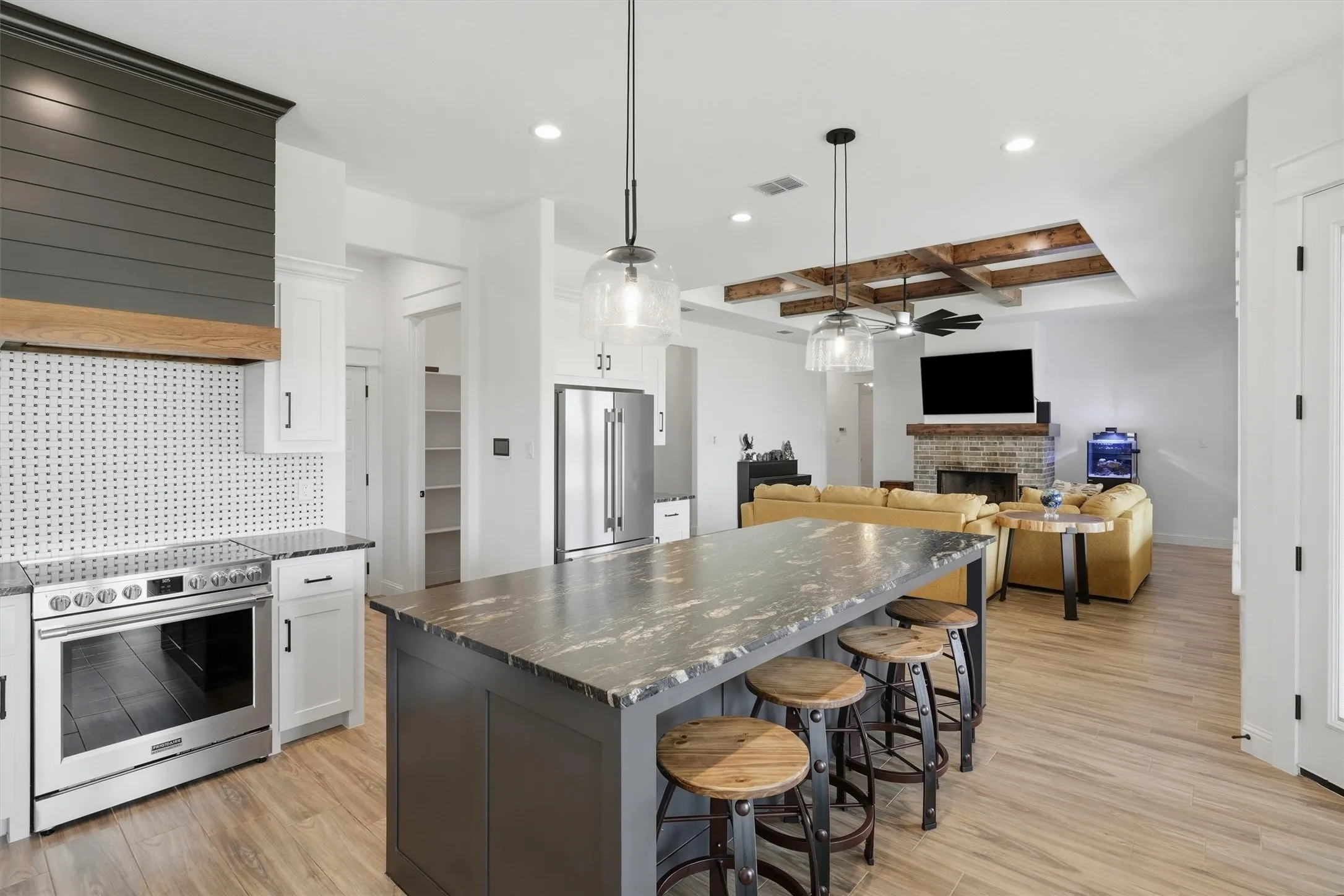 Spacious open-concept layout featuring wood-finish flooring, a kitchen island with stone countertop, stainless steel appliances, and a recessed ceiling with exposed wood beams