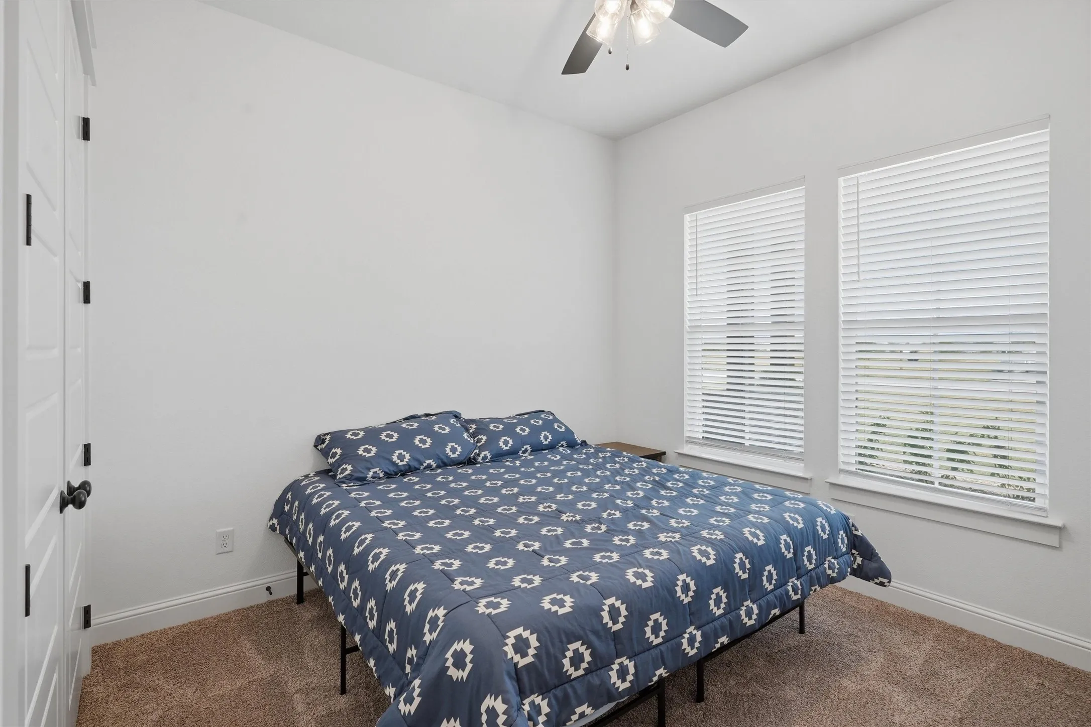 Two windows with blinds, ceiling fan, and carpet flooring