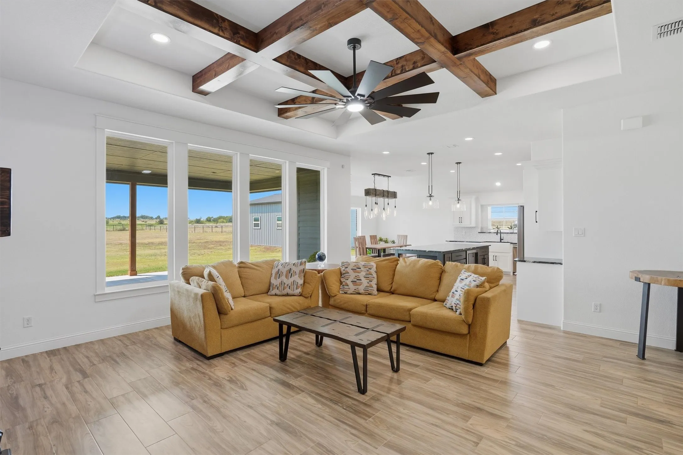 Spacious living area featuring wood-finish flooring, a coffered ceiling with exposed wood beams, and a ceiling fan