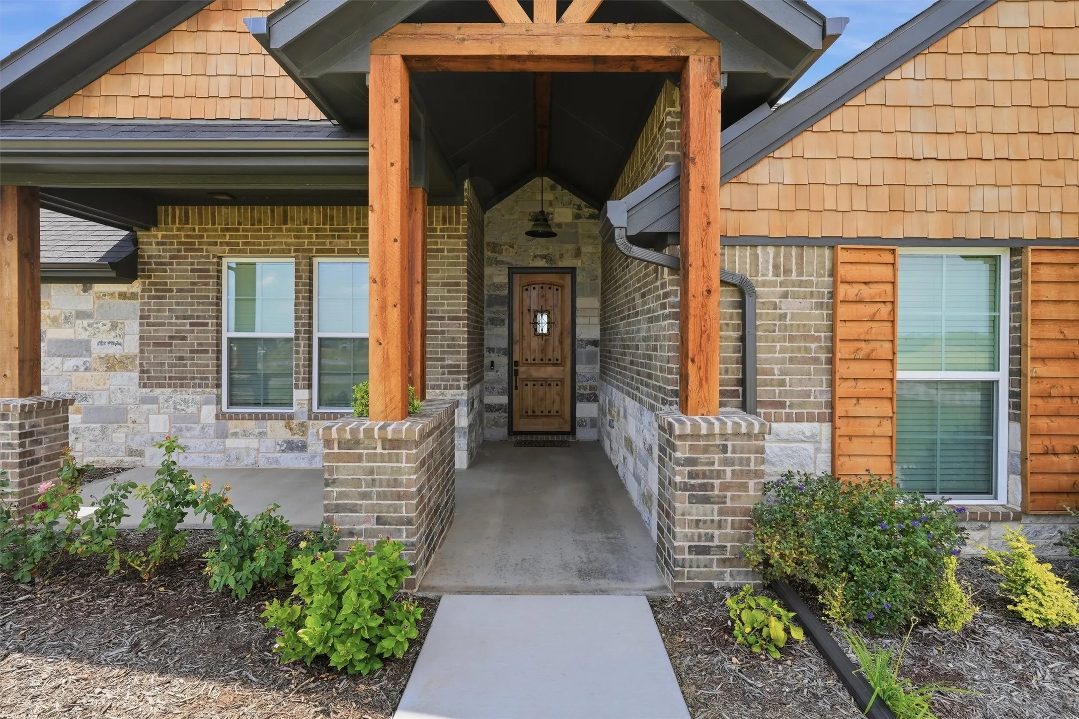 Brick and stone exterior with cedar shake siding, wood-framed entry, and a wood-paneled front door with decorative ironwork
