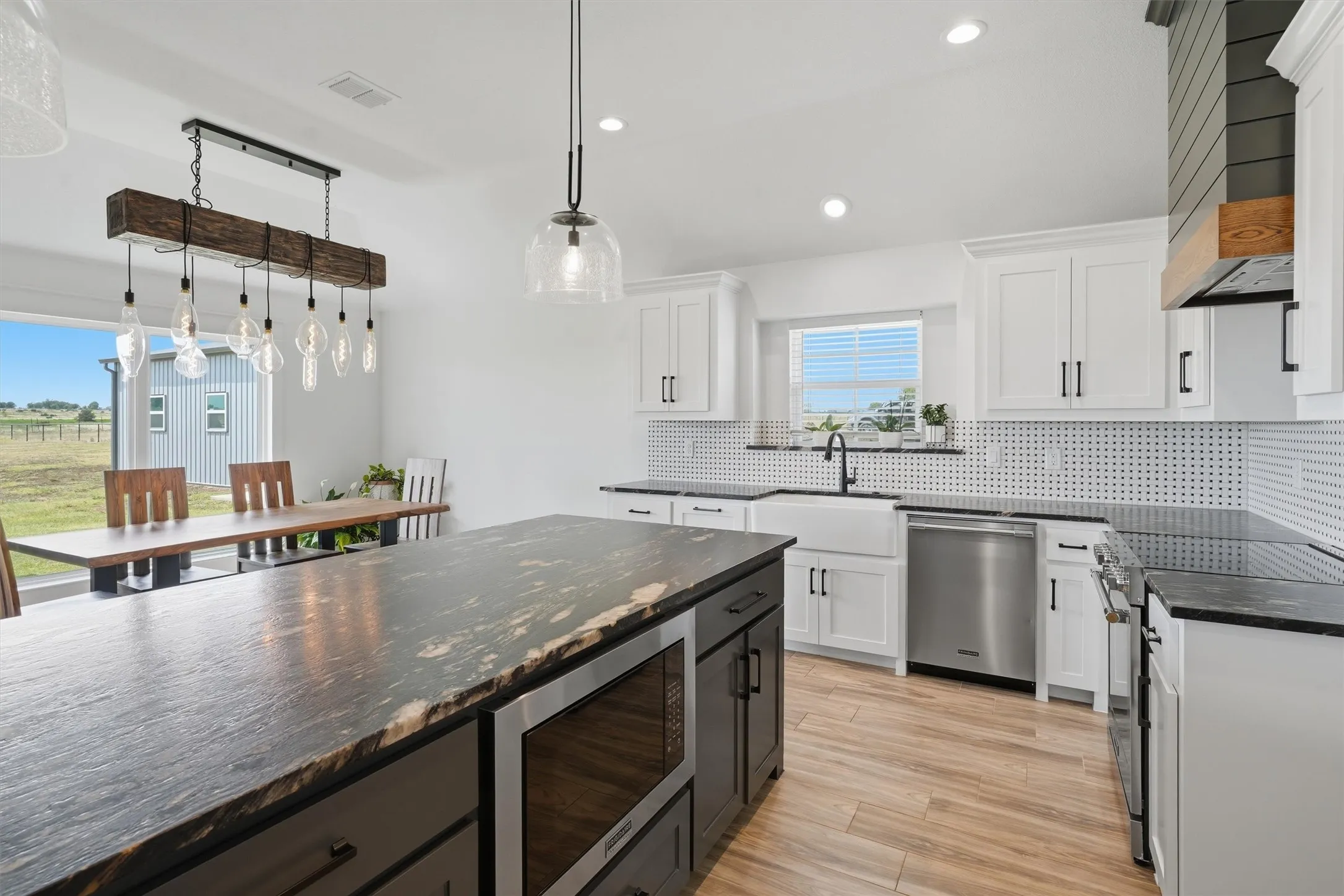 Spacious kitchen featuring an expansive island with stone-finish countertop, white cabinetry with black hardware, stainless steel appliances, and a farmhouse sink