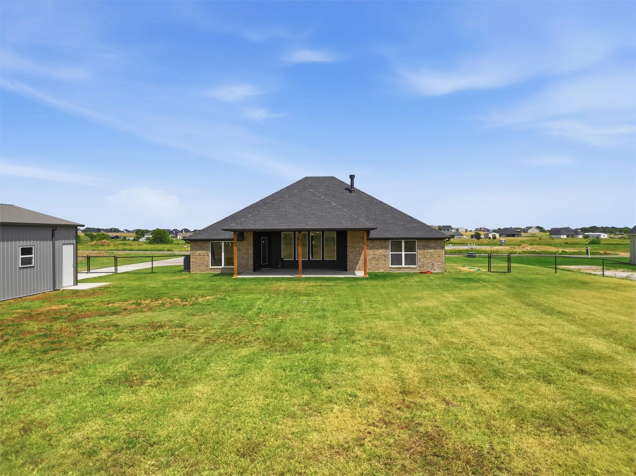 Spacious rear yard with a covered patio, brick exterior, dark roof, and a separate metal outbuilding