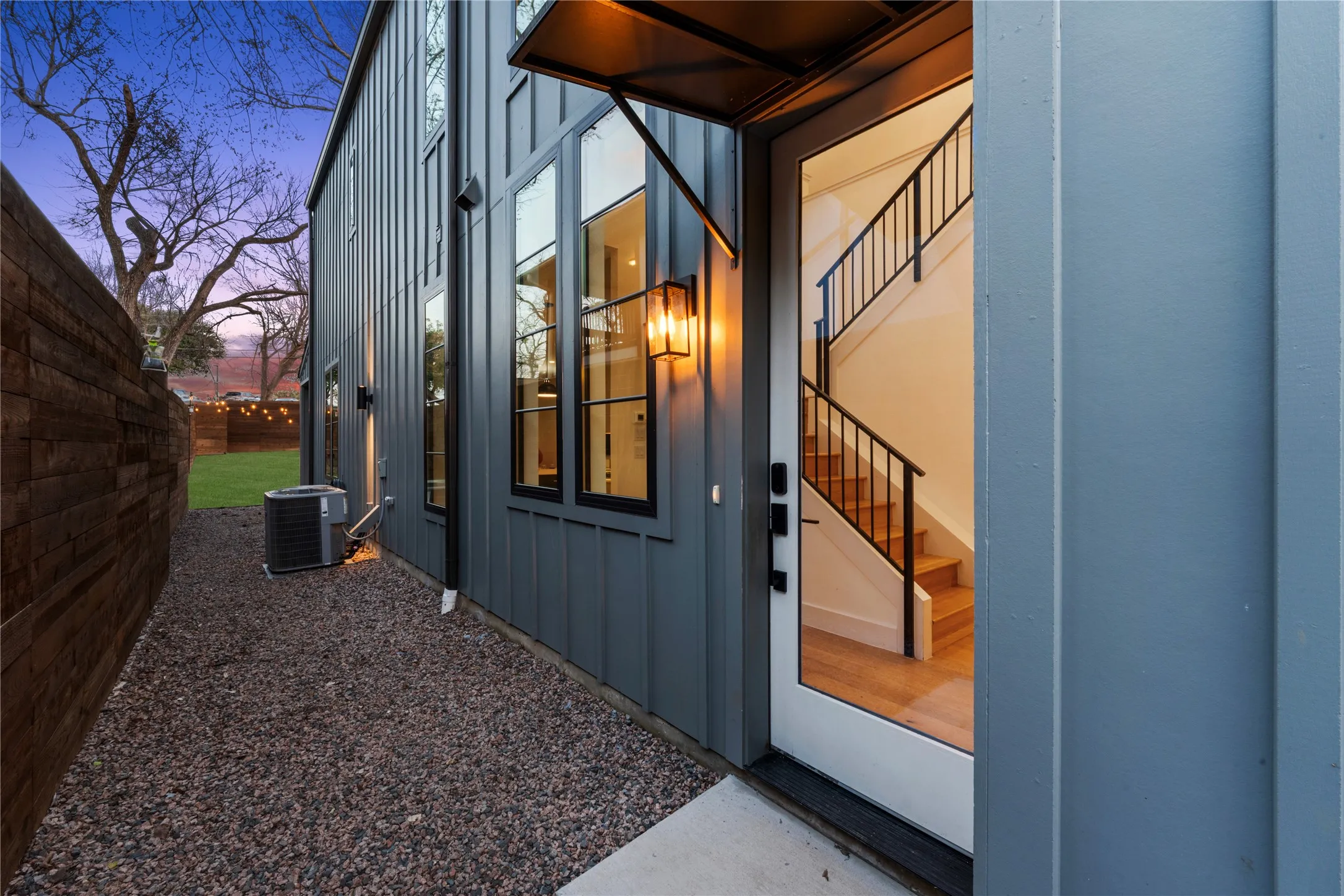 Board and batten exterior with multiple tall windows, a gravel side yard, and a wooden privacy fence