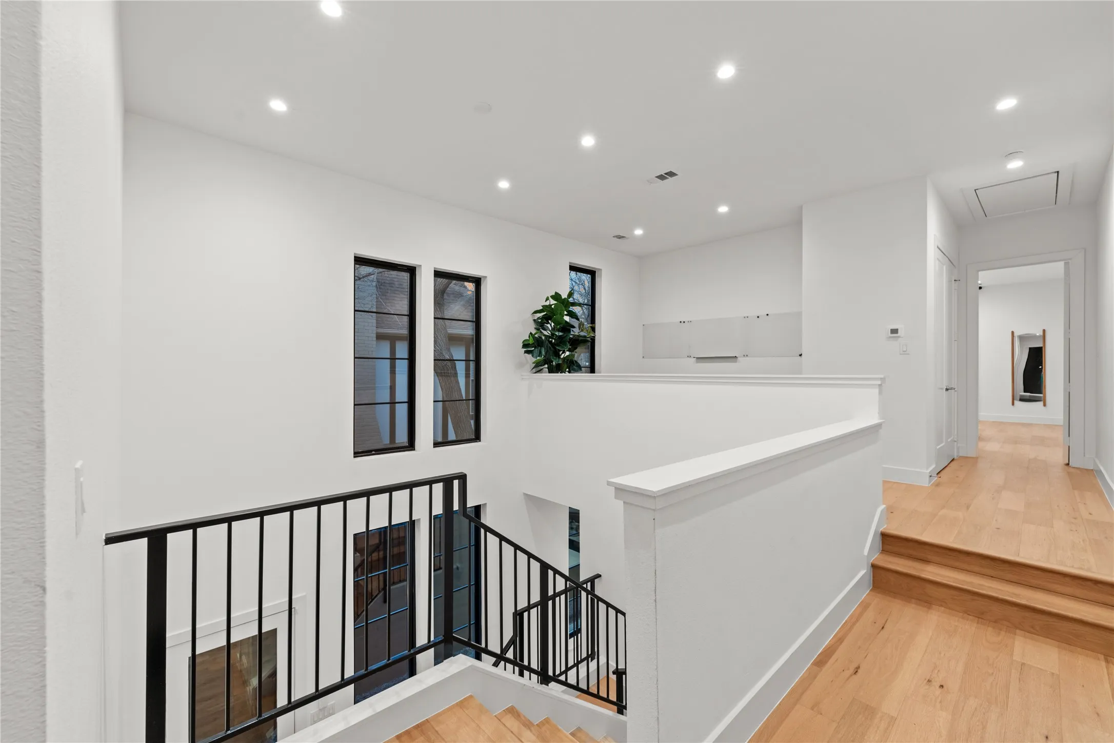 Recessed lighting, wood-finish flooring, white walls, black-framed windows, and black metal railings