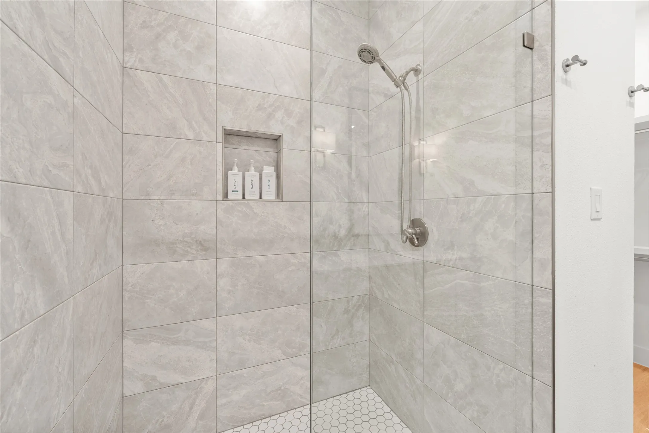 Walk-in shower featuring light-toned tile, built-in niche, and brushed nickel fixtures