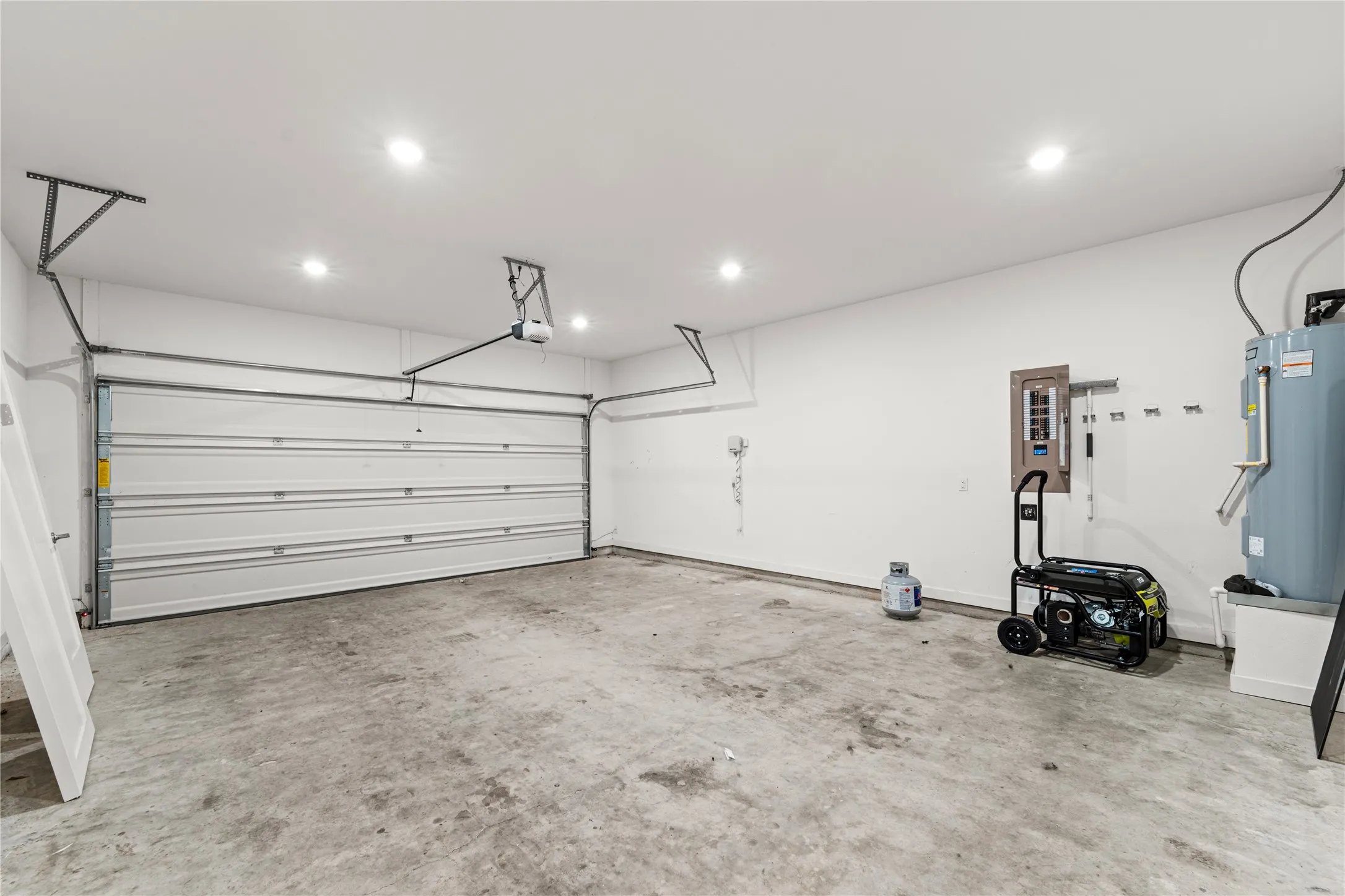 Spacious front facing two-car garage with an overhead door, concrete flooring, recessed lighting.