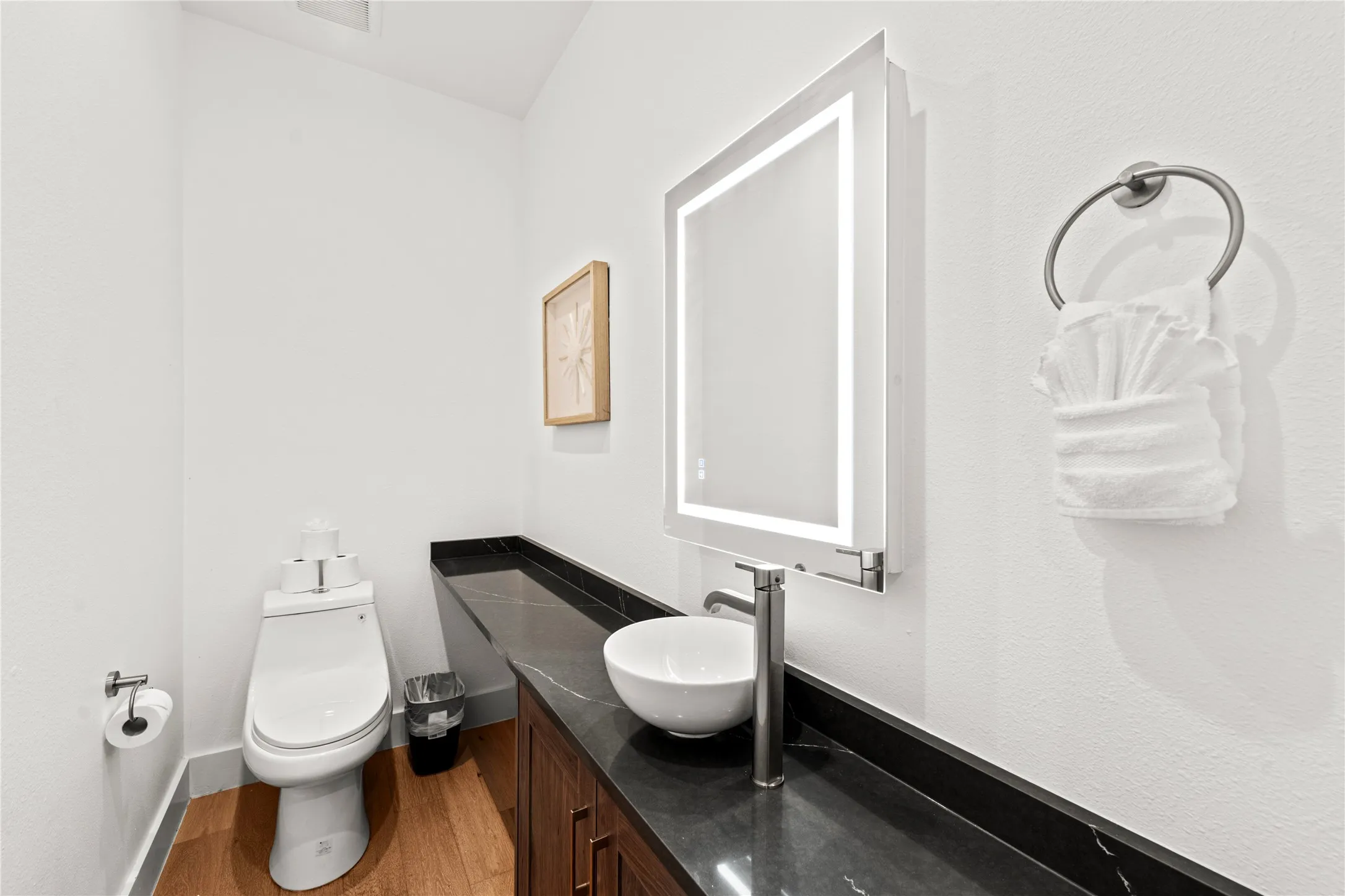 Floating vanity with a vessel sink, dark countertop, and an illuminated mirror