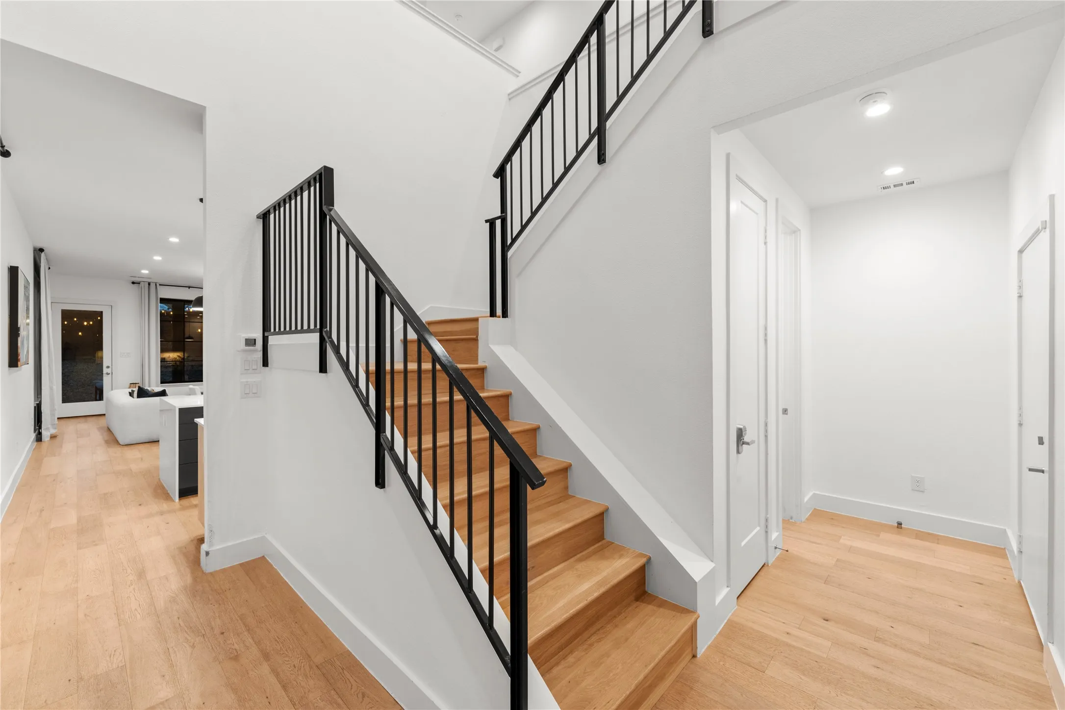 Wood-finish flooring, staircase with natural wood treads and black metal railing, recessed lighting, and white paneled doors