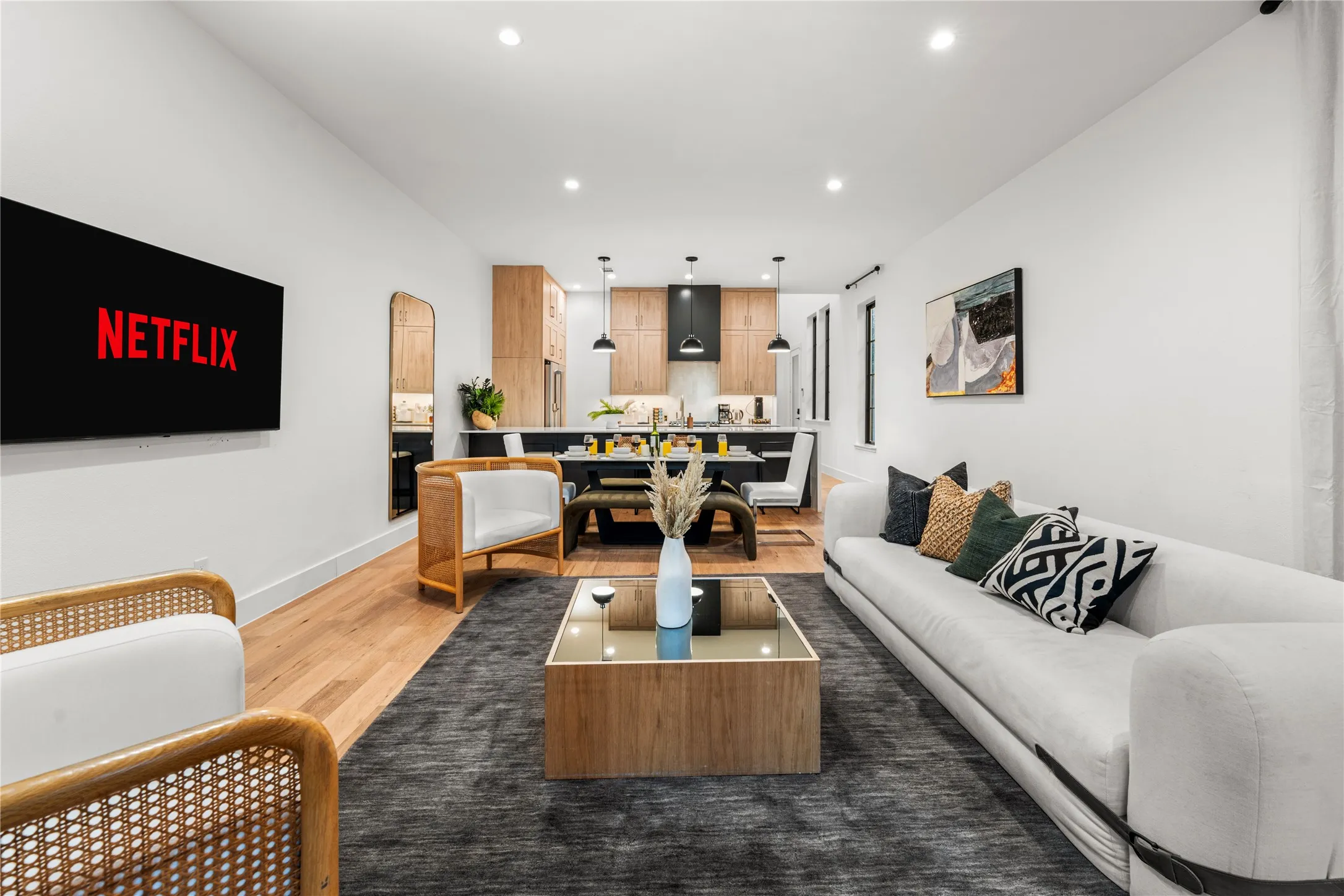Open-concept living space featuring wood-finish flooring, recessed lighting, and a kitchen with light wood cabinetry and a dark range hood