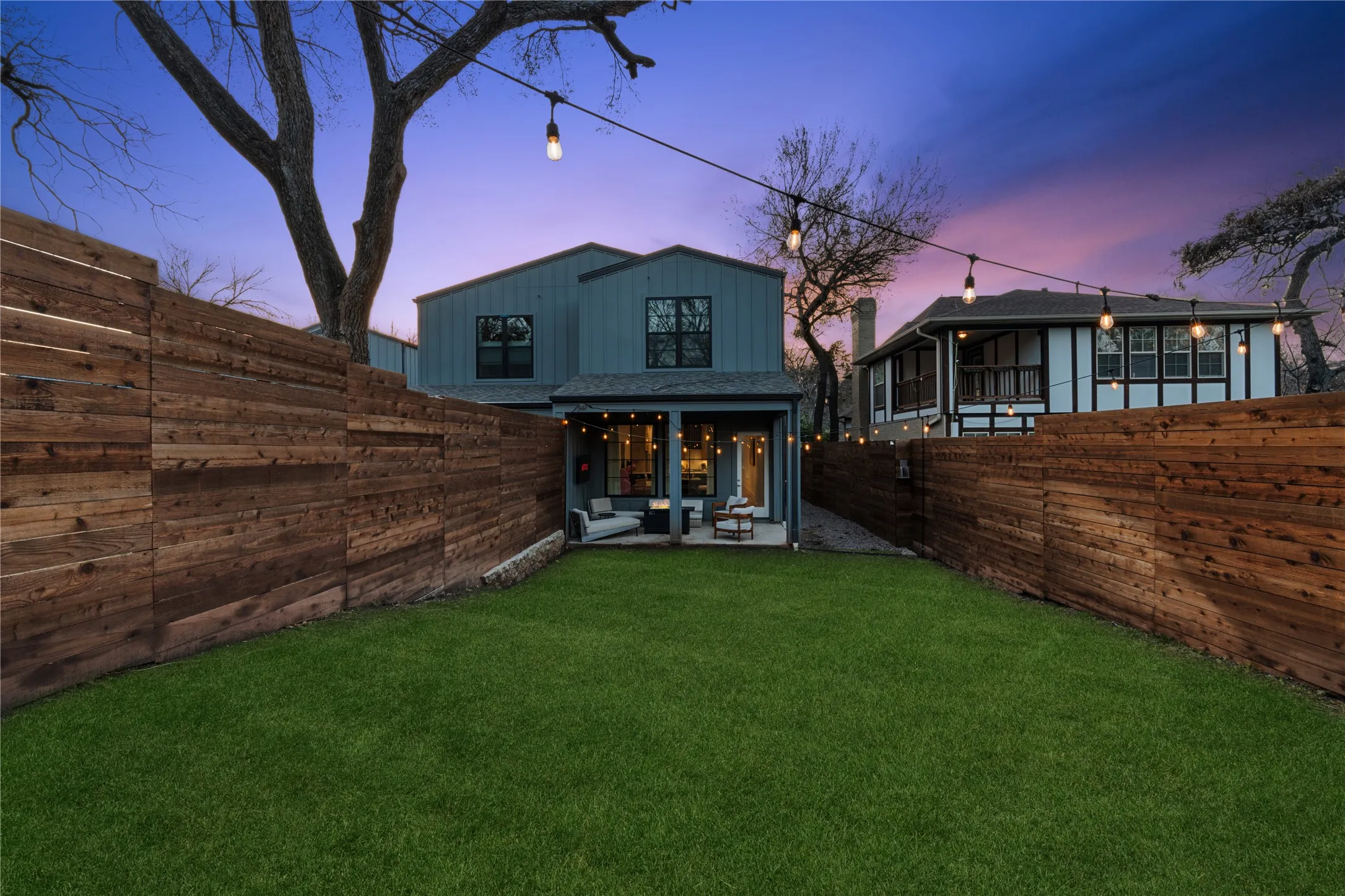 Expansive backyard with a manicured lawn, a full-width wood privacy fence, and string lighting