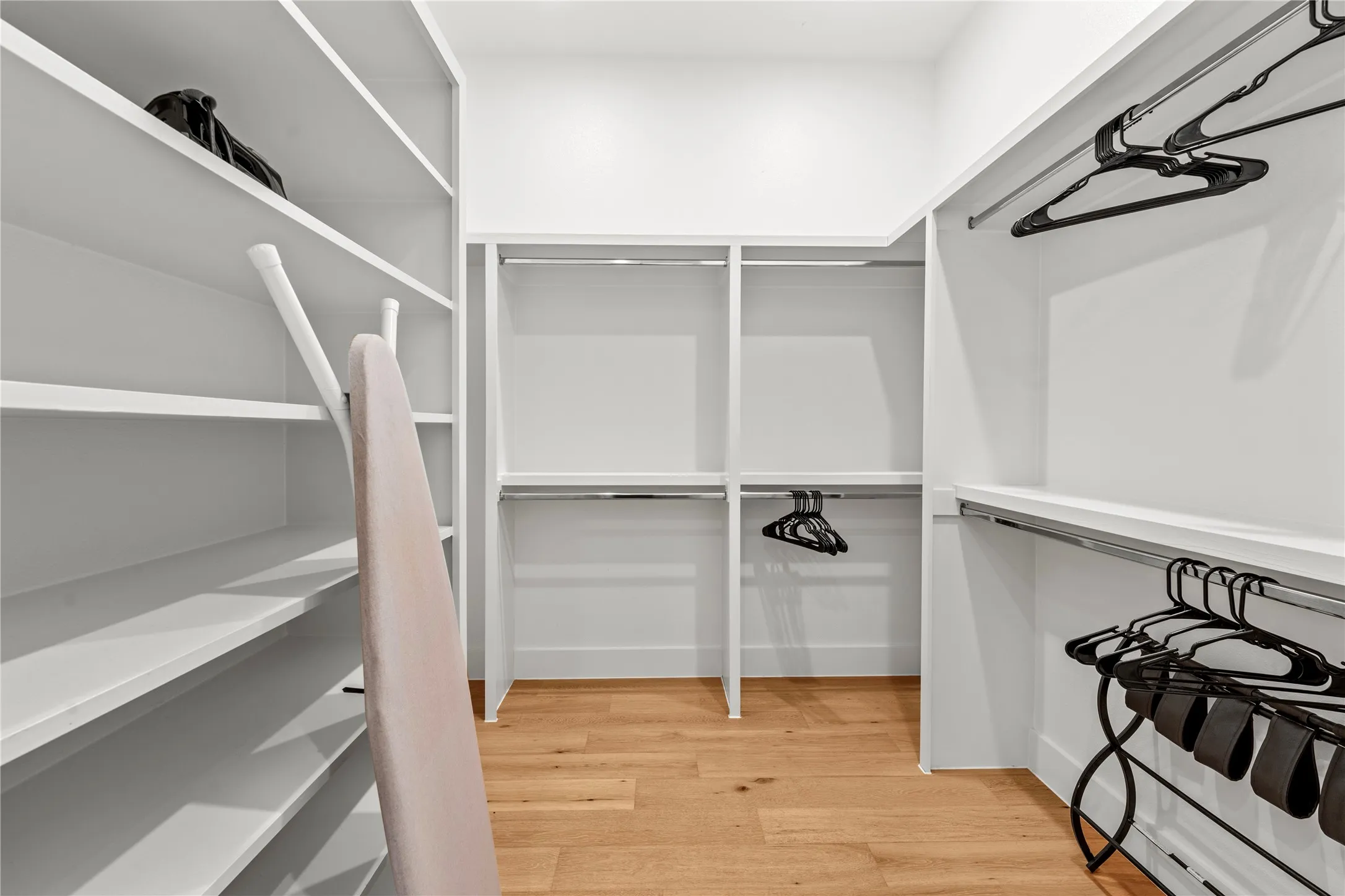 Built-in white shelving, chrome hanging rods, and wood-finish flooring