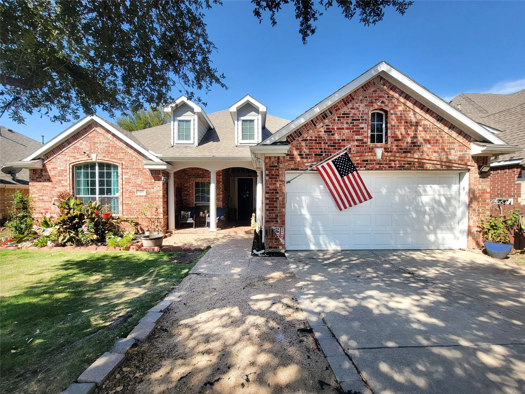 Brick exterior with dormer windows, an arched entry, a covered porch, a two-car garage, and a concrete driveway