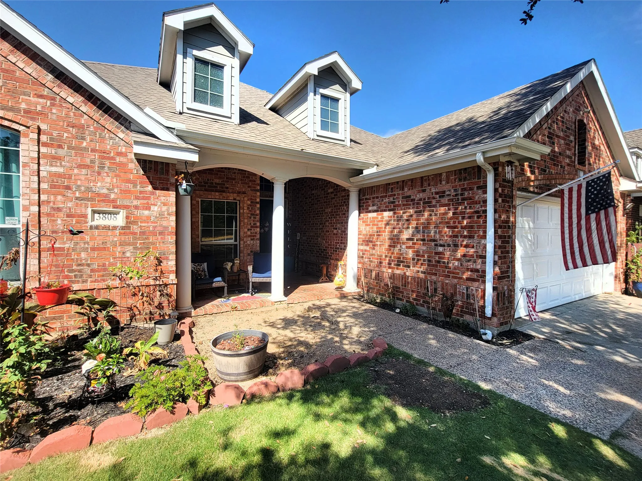 Brick exterior with dormer windows, covered front entry, attached garage, and concrete driveway
