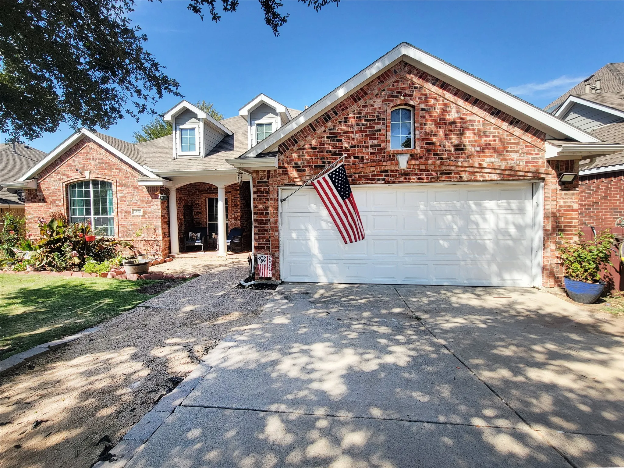 Red brick exterior with white trim, arched entryway, dormer windows, and attached garage