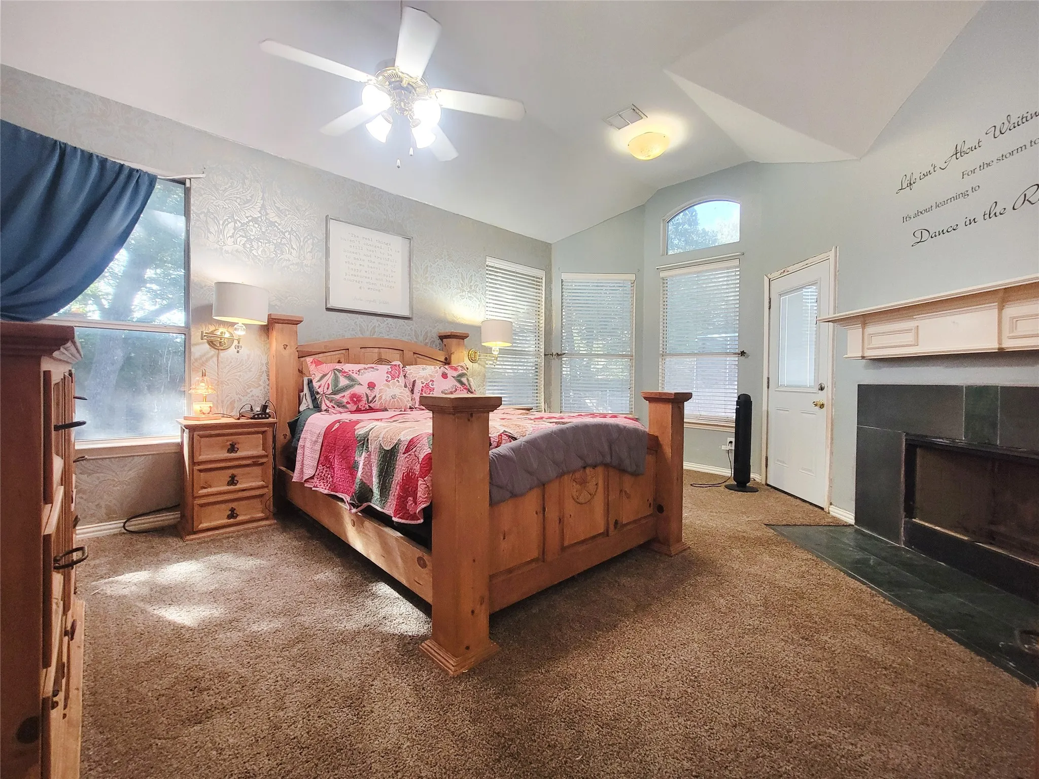 Vaulted ceiling with ceiling fan, multiple windows with blinds, recessed lighting, and a fireplace with a mantel, private door to backyard