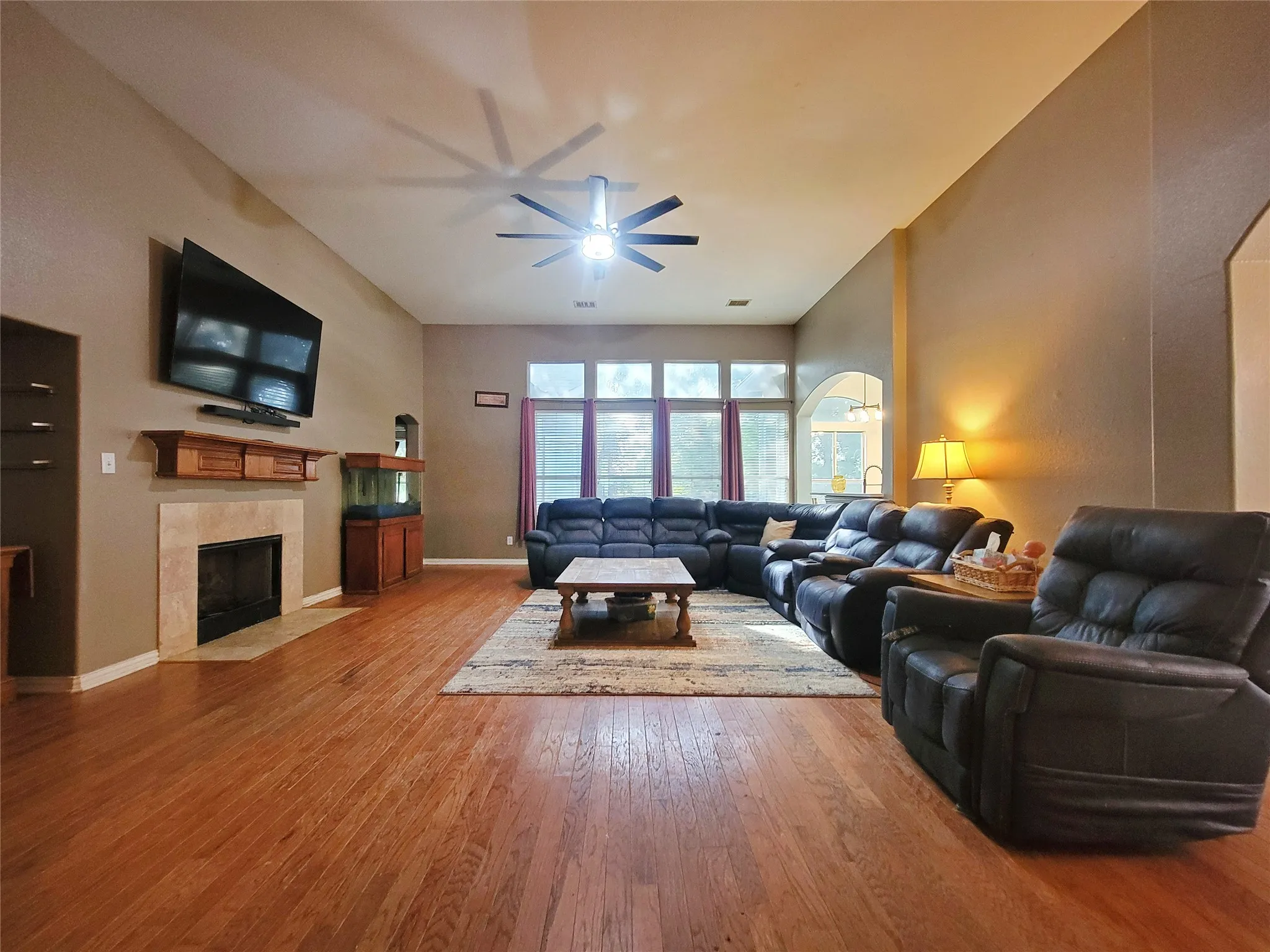 Vaulted ceiling with an attached fan, wood-finish flooring, a fireplace with a stone surround, and large windows