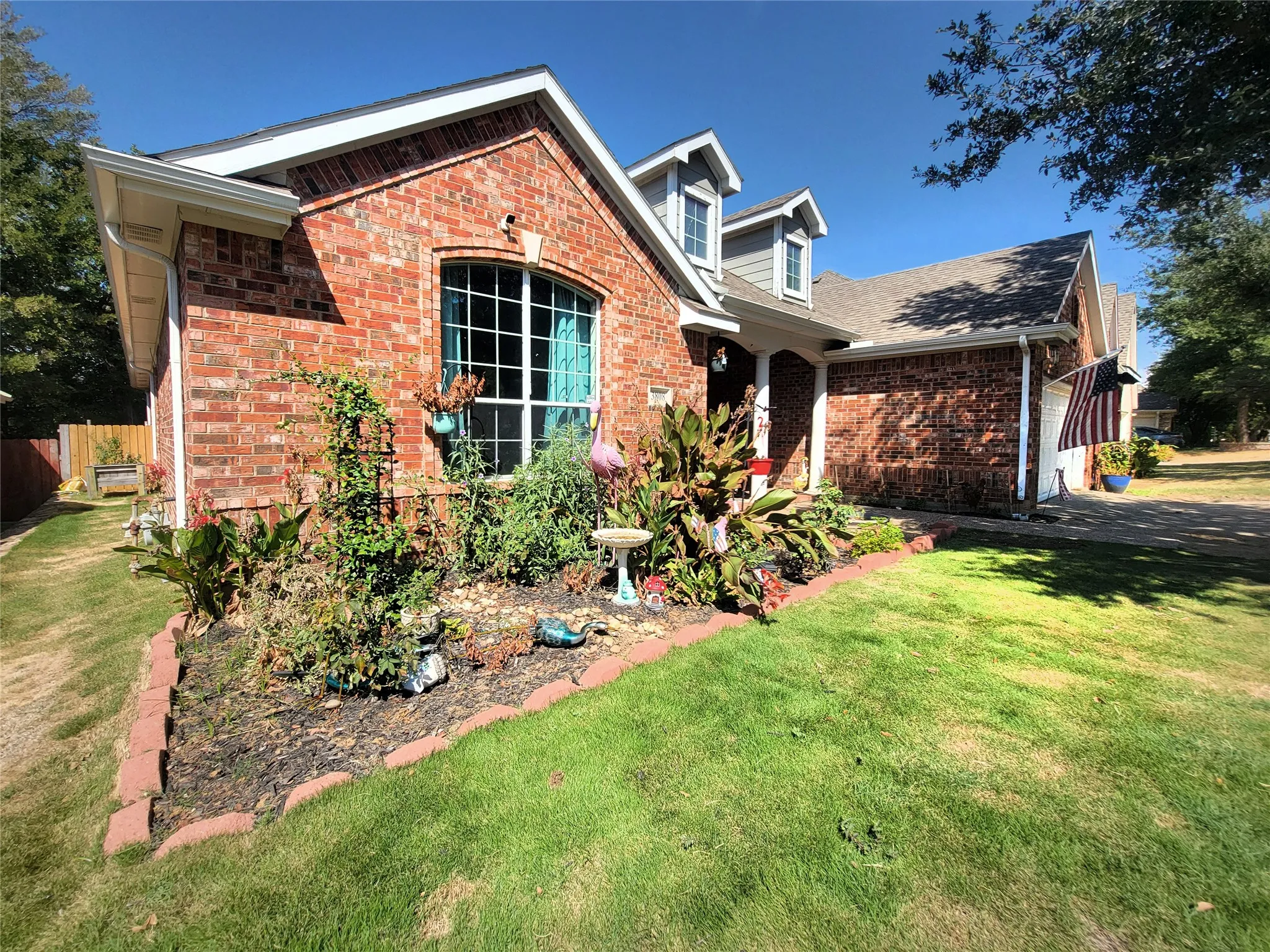 Brick exterior with white trim, arched window, front landscaping with brick edging, dormer windows, and a paved driveway