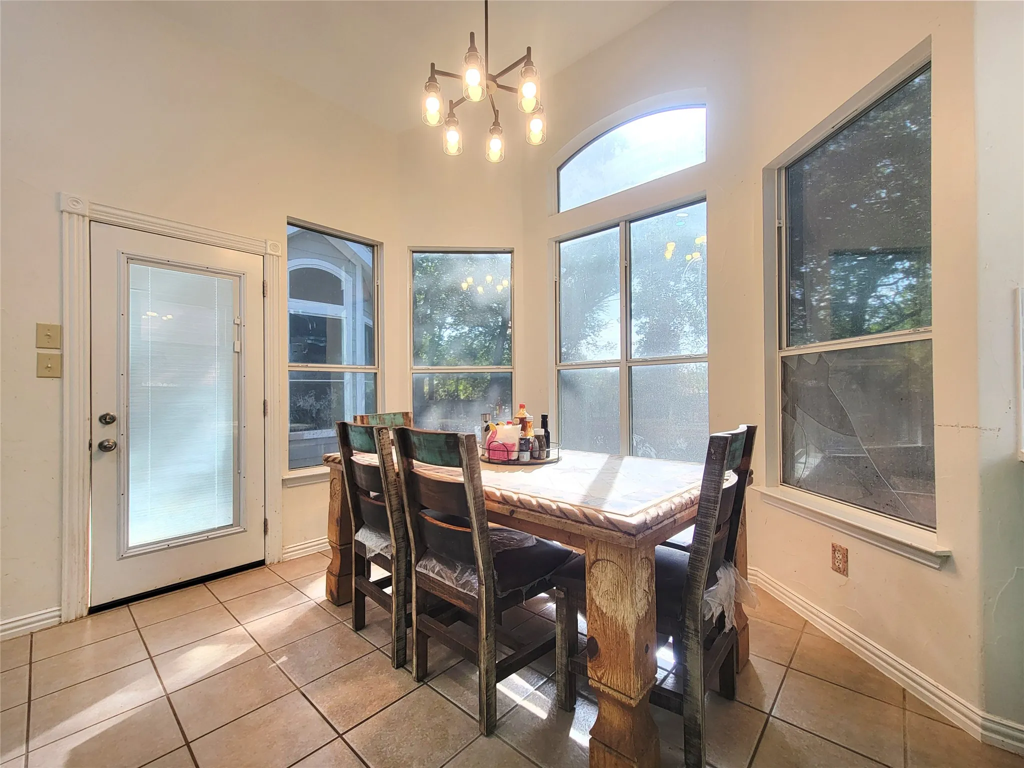 Vaulted ceiling with an architectural chandelier, arched transom window, multiple large windows, and tile flooring