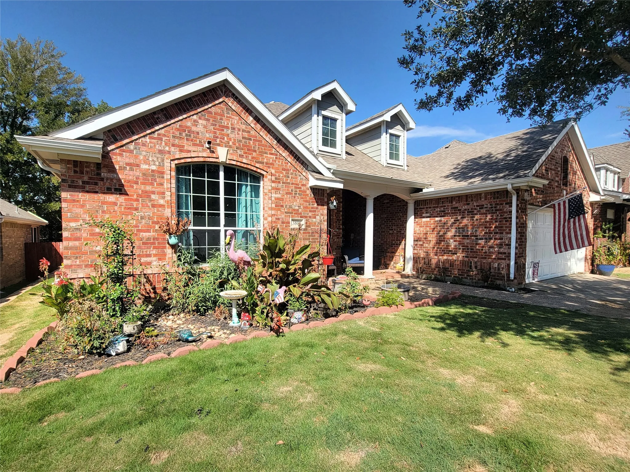 Brick exterior with dormer windows, an arched entry, and an attached garage