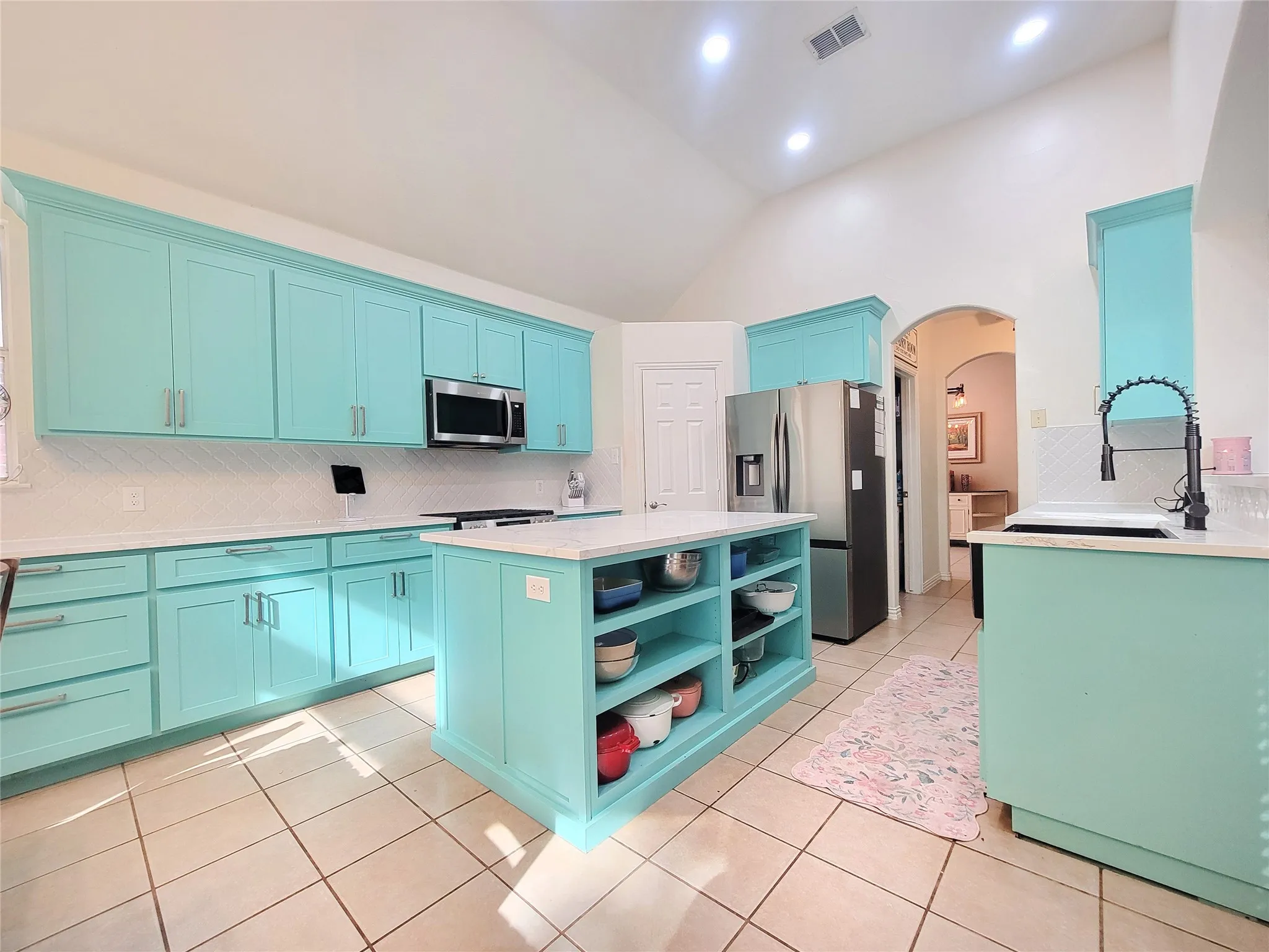 Vaulted ceiling kitchen featuring turquoise cabinetry, a center island with open shelving, tile flooring, and stainless steel appliances
