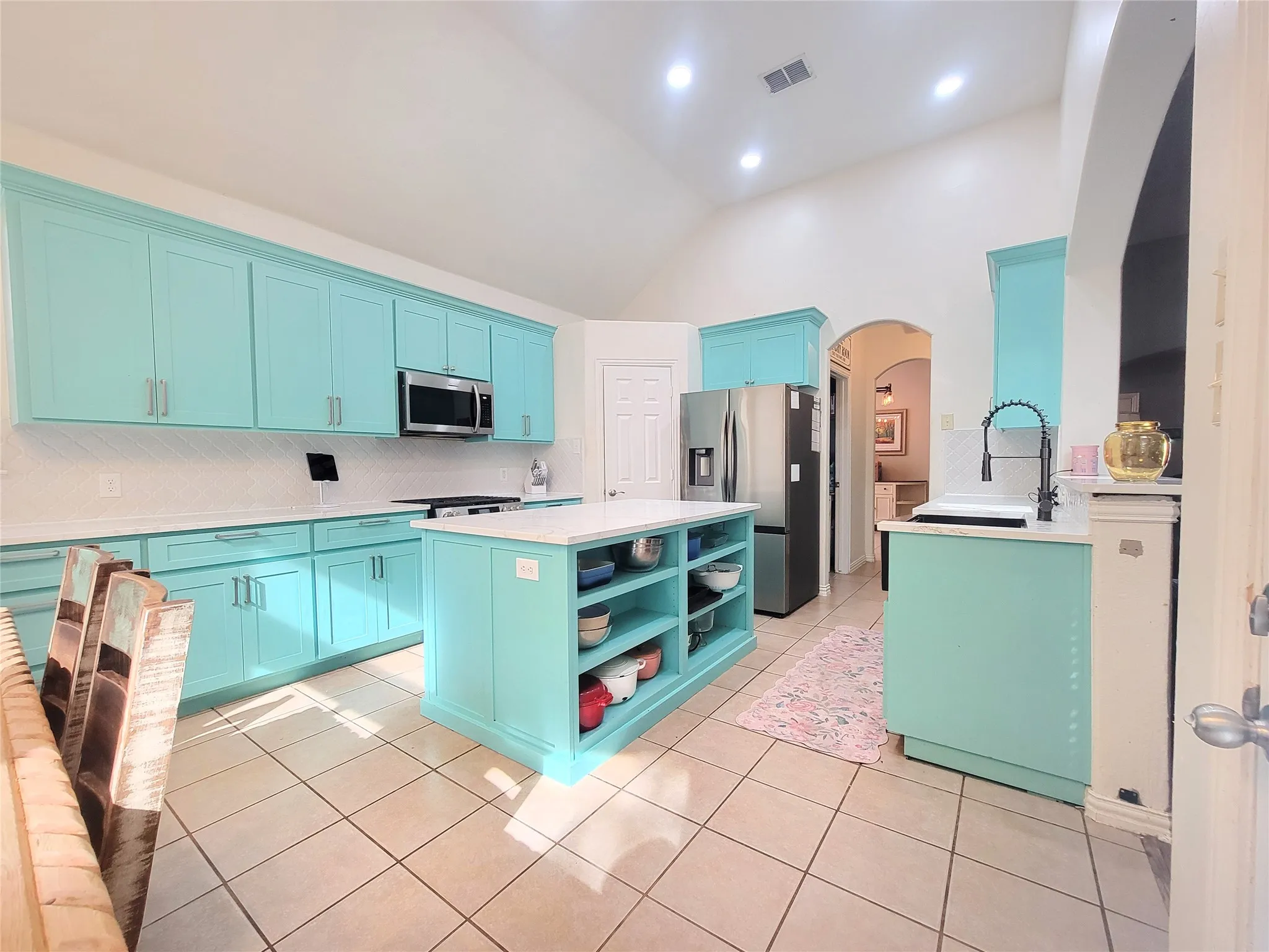 Vaulted ceiling kitchen featuring an island with open shelving, recessed lighting, tile flooring, and stainless steel appliances