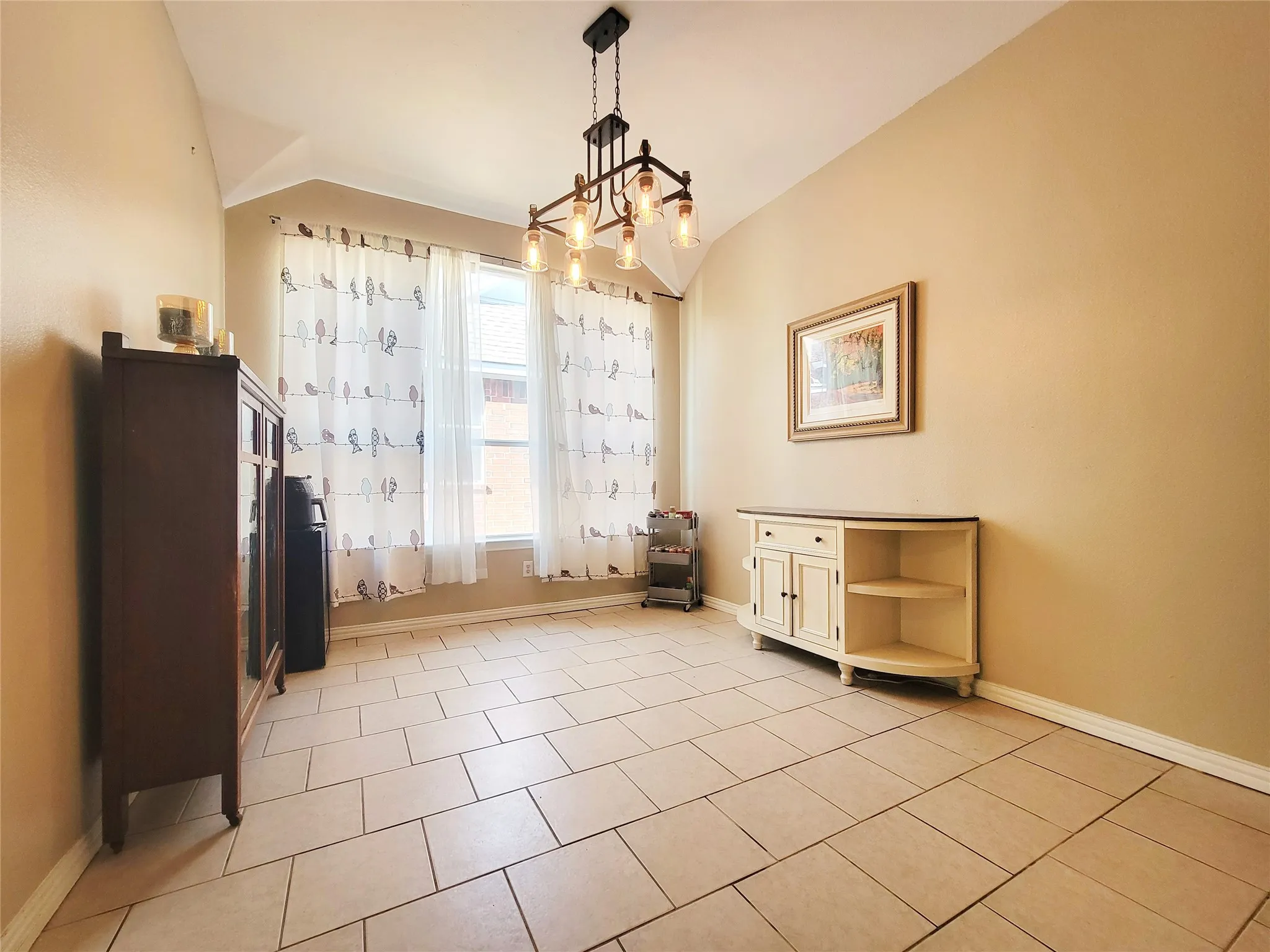 Vaulted ceiling, two windows, suspended multi-bulb light fixture, and light-toned tile flooring