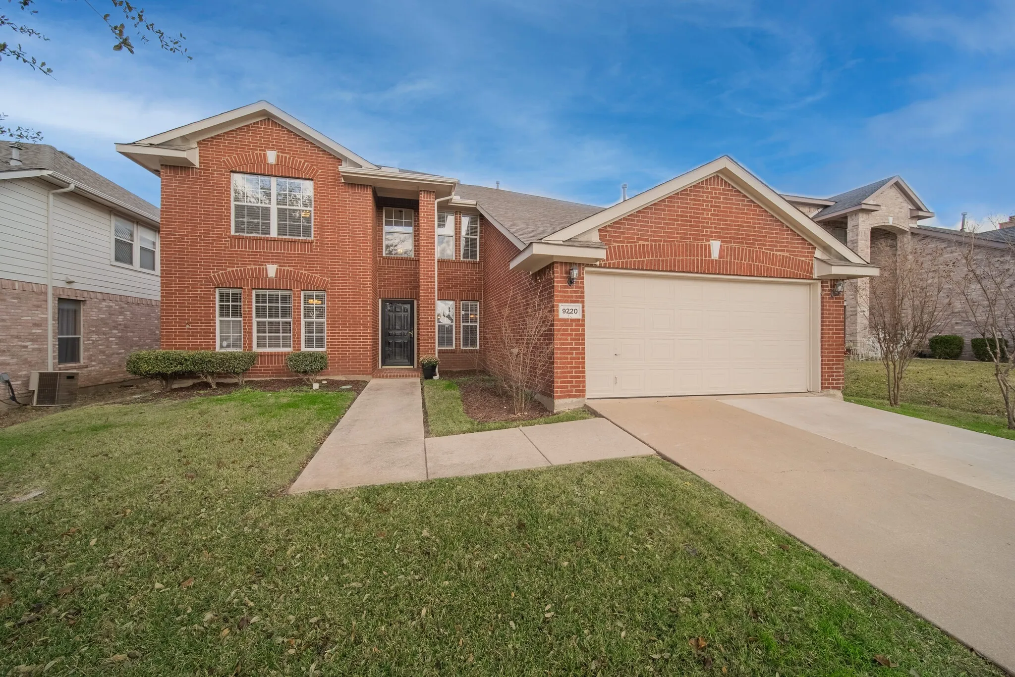 Brick facade, multi-pane windows, two-car garage, concrete driveway, and front walk
