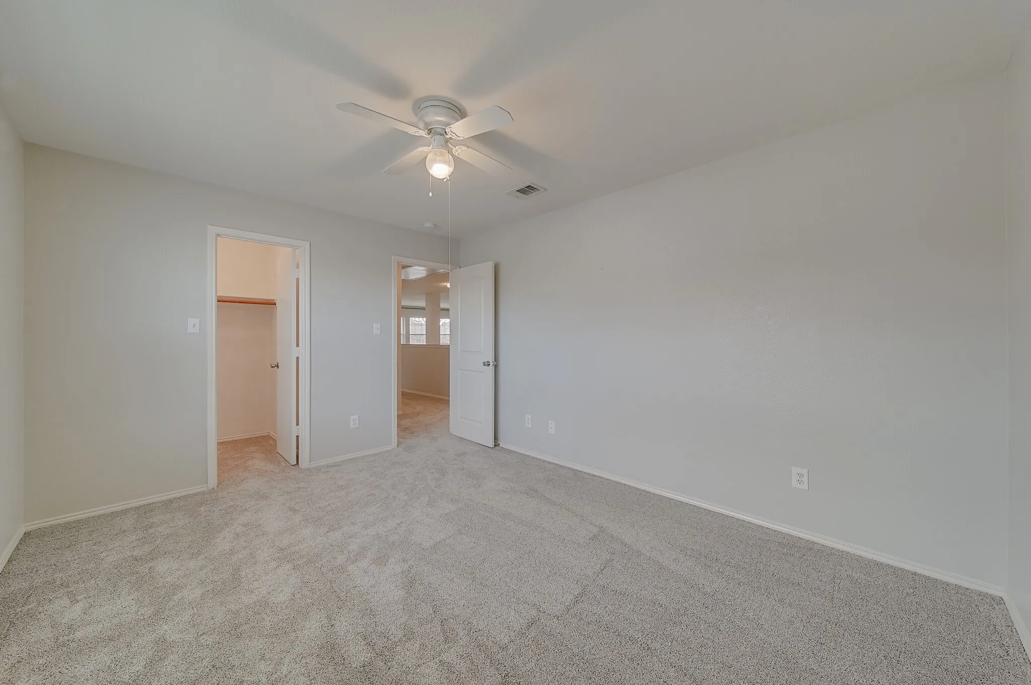 Neutral gray walls, light gray carpet flooring, ceiling fan with integrated light, walk-in closet with built-in hanging rod, white interior doors
