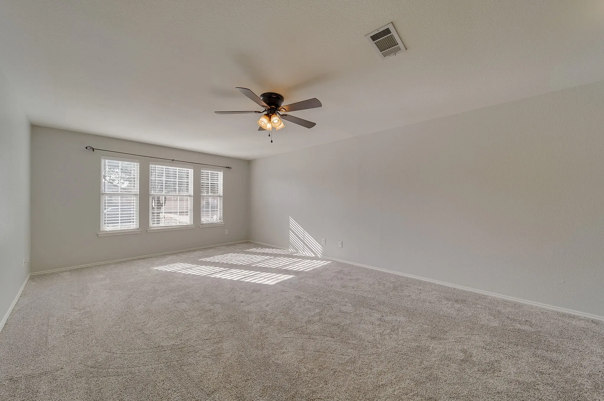 Expansive room featuring carpet flooring, three windows with horizontal blinds, and a ceiling fan with integrated lighting
