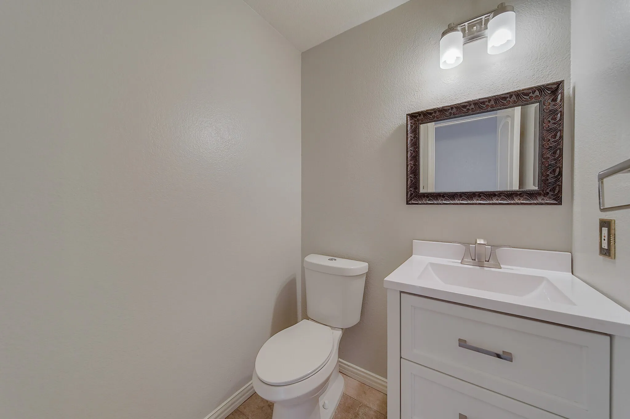 Corner vanity with a white countertop and integrated sink, framed mirror, and two-light fixture