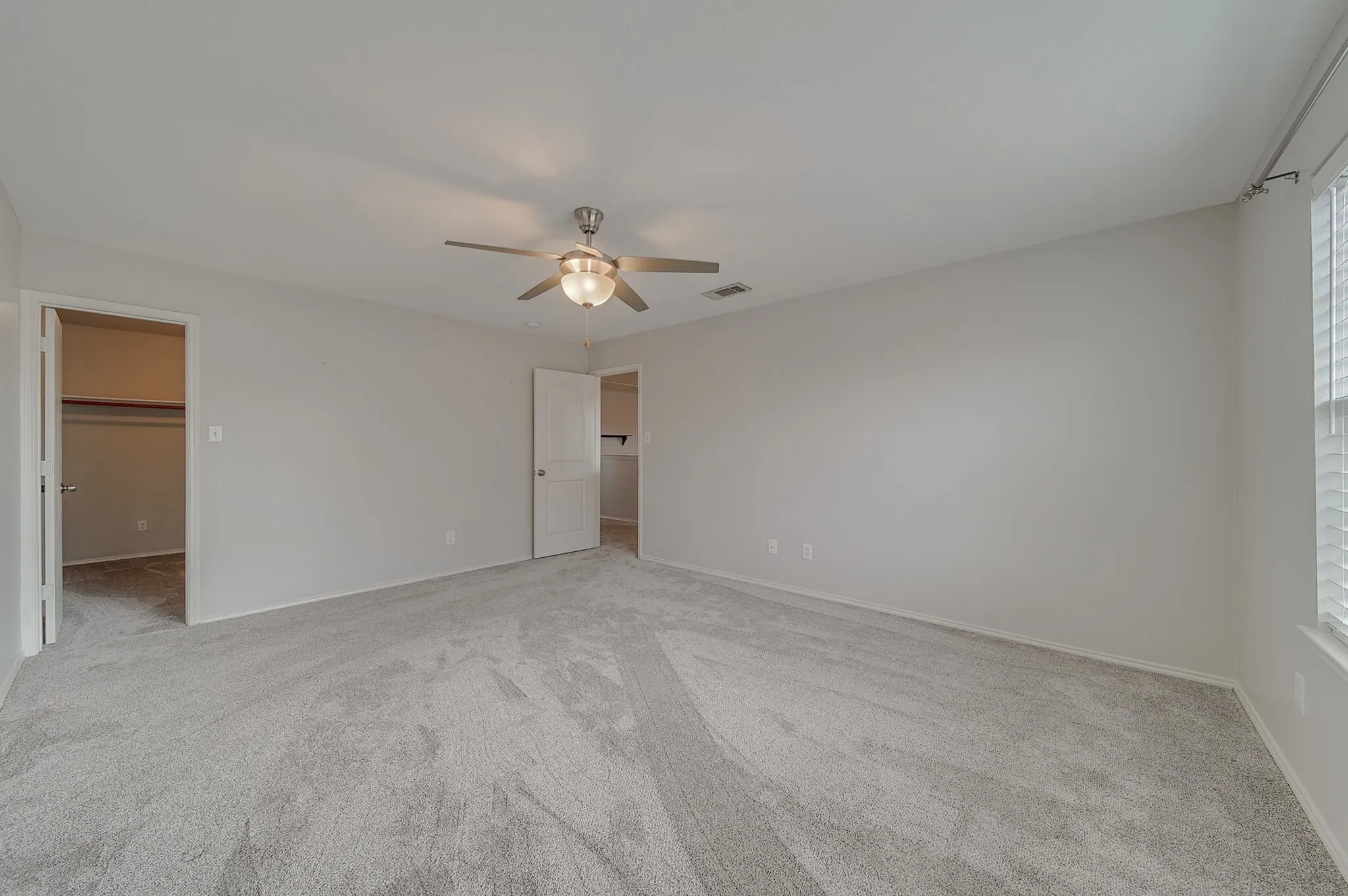 Spacious room with light-colored carpeting, a ceiling fan with integrated lighting, and a window featuring horizontal blinds