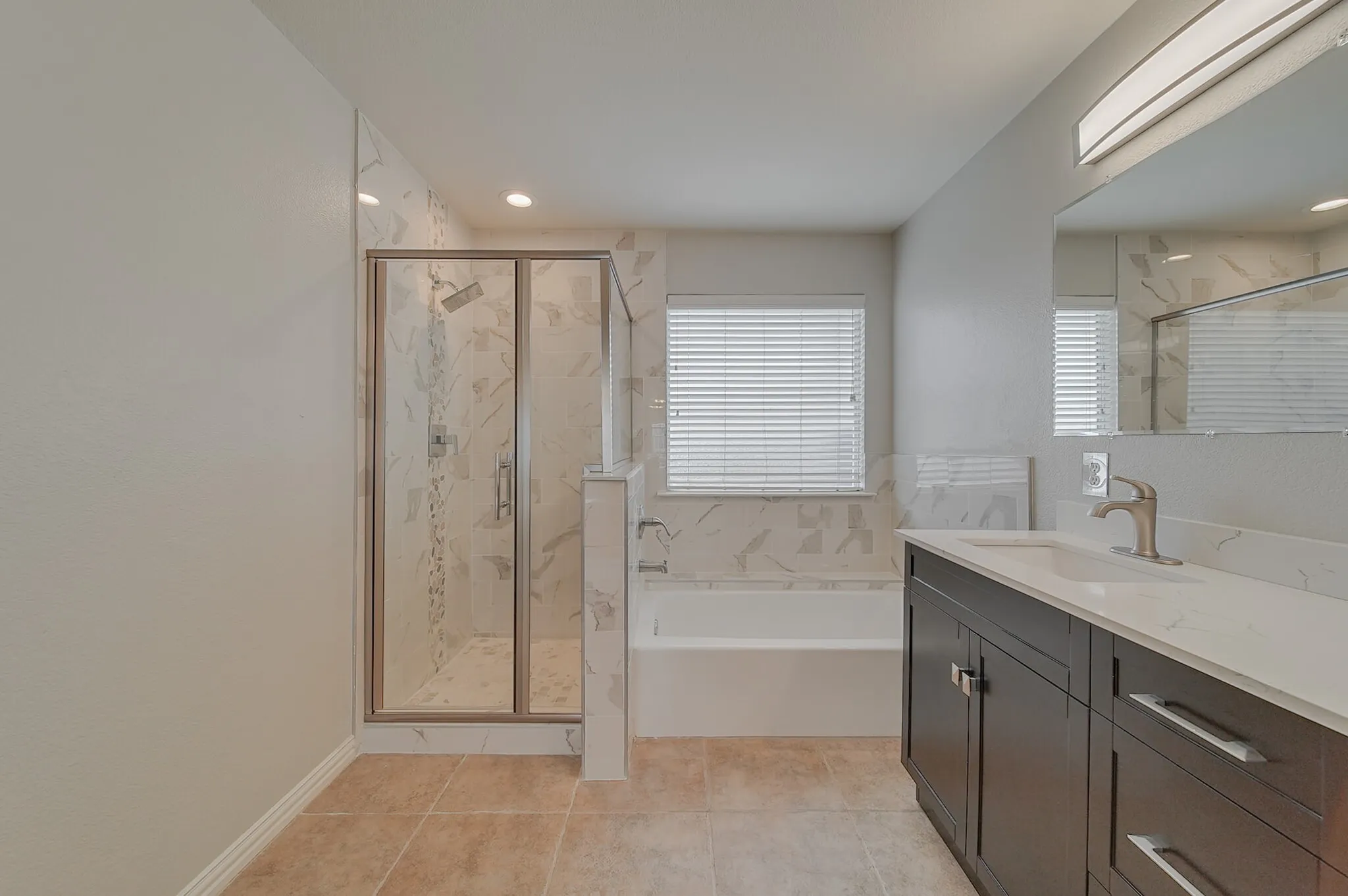 Walk-in shower with glass enclosure, separate soaking tub, dark wood-finish vanity with countertop, brushed nickel fixtures, and tiled flooring