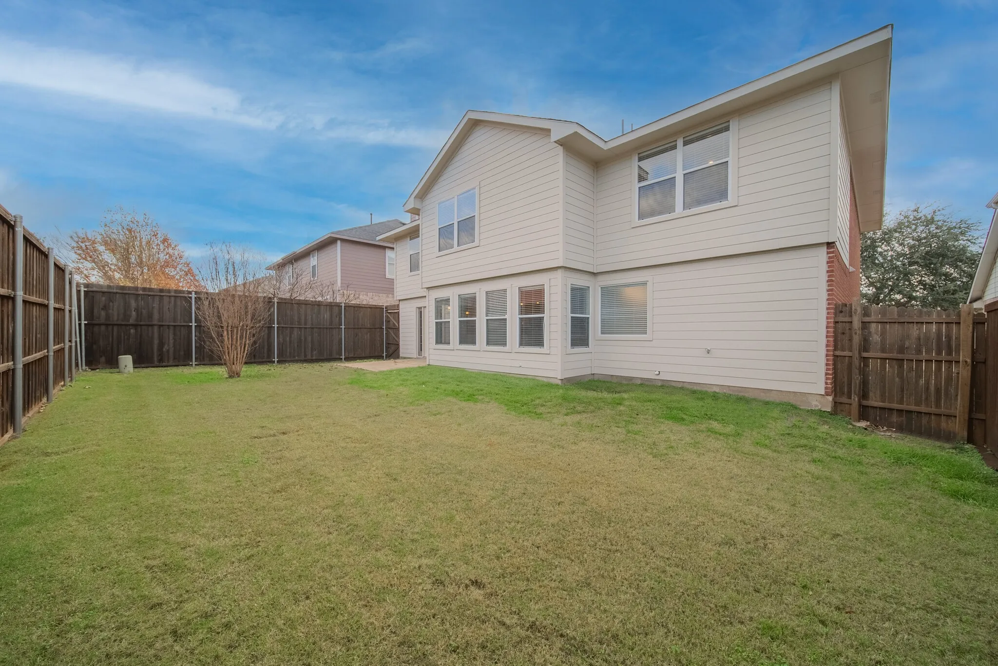 Expansive backyard with a manicured lawn, full perimeter privacy fencing, and a concrete patio